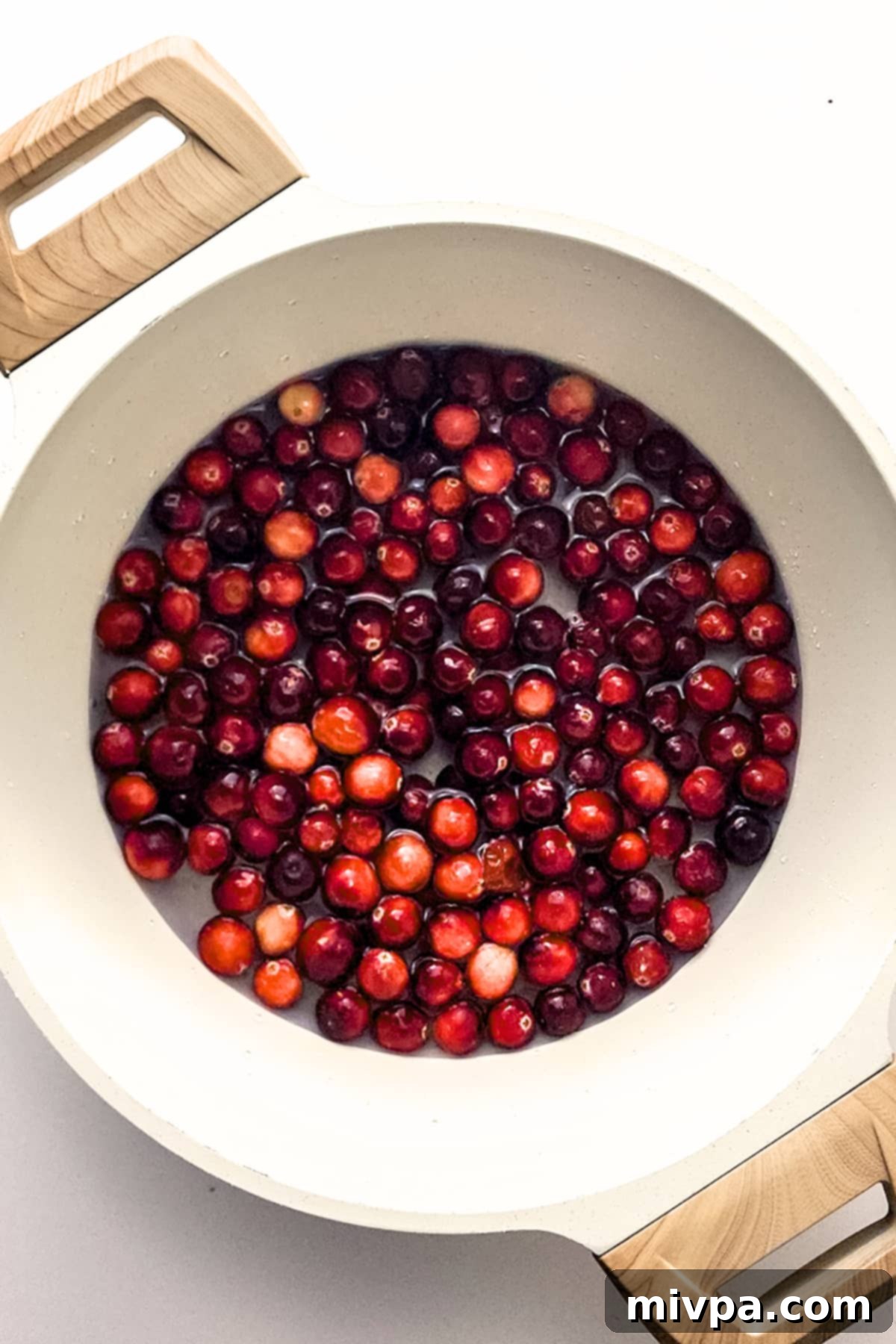 Fresh cranberries boiling vigorously in a pot of water on the stove, releasing their vibrant color.