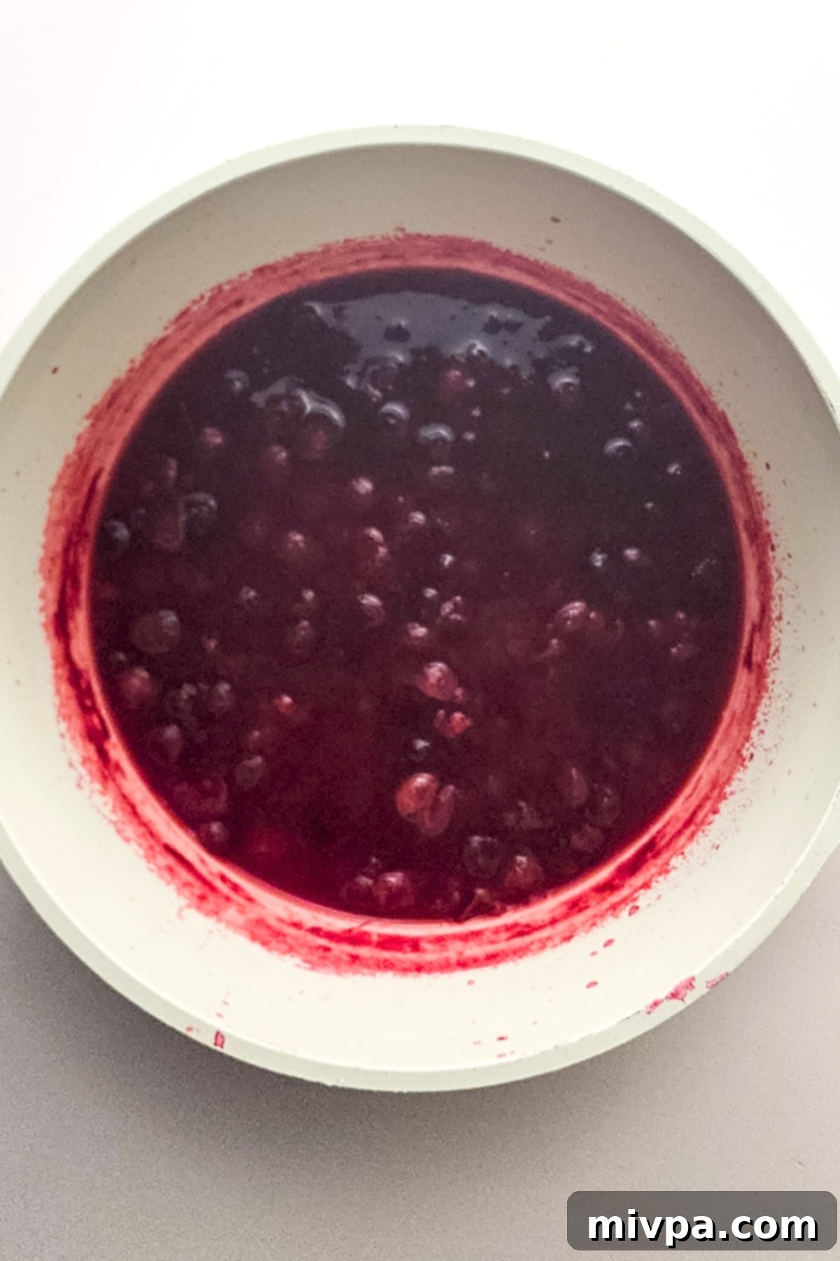 Cranberry juice simmering gently in a covered pot on low heat, showcasing its deepening red color.