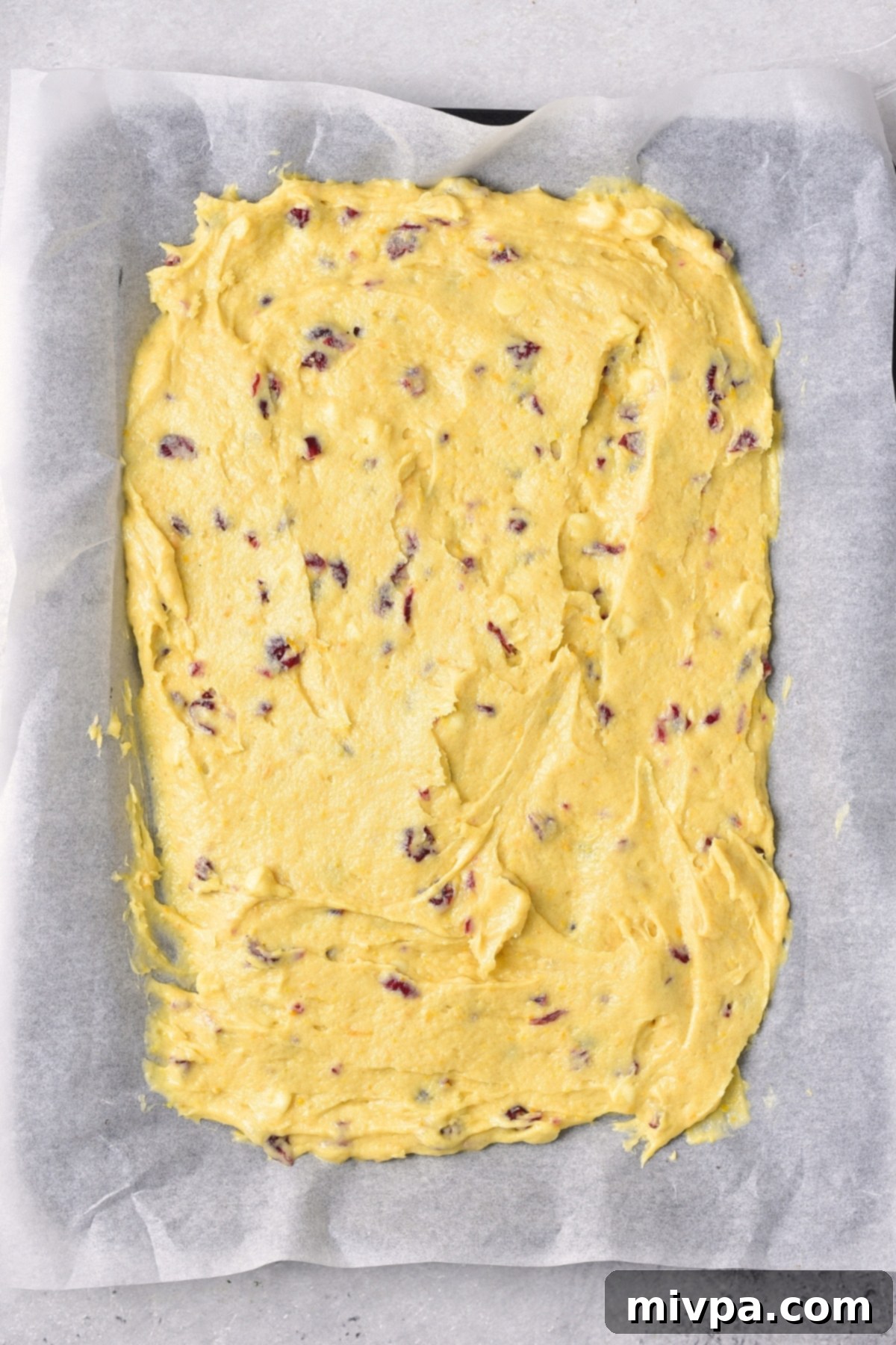 White Chocolate Cranberry Bars (Gluten-Free, Dairy-Free Baking) Smoothly spread cranberry cake batter on a parchment-lined baking pan, ready for the oven.