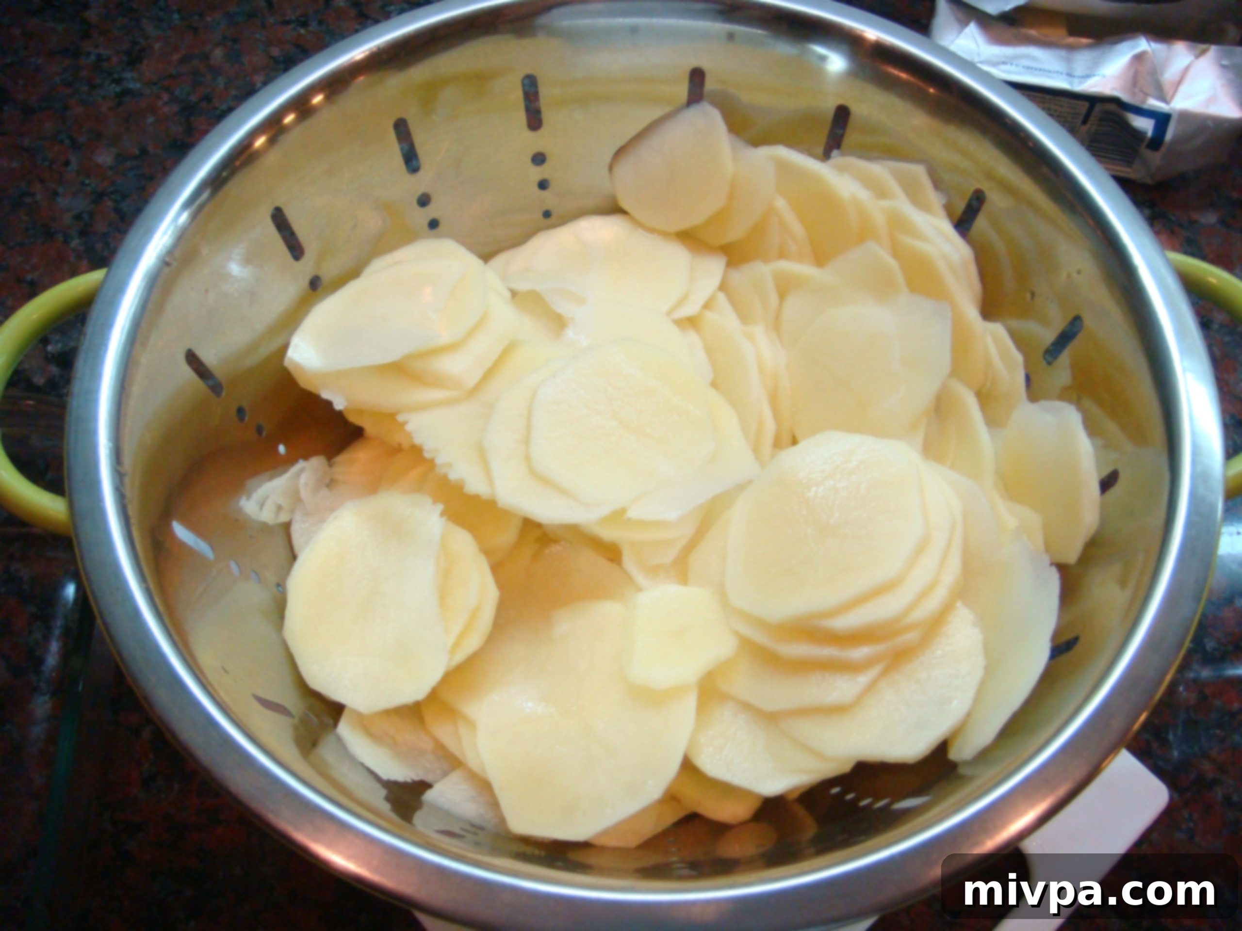 Thinly sliced potatoes on a mandoline slicer, ready for layering