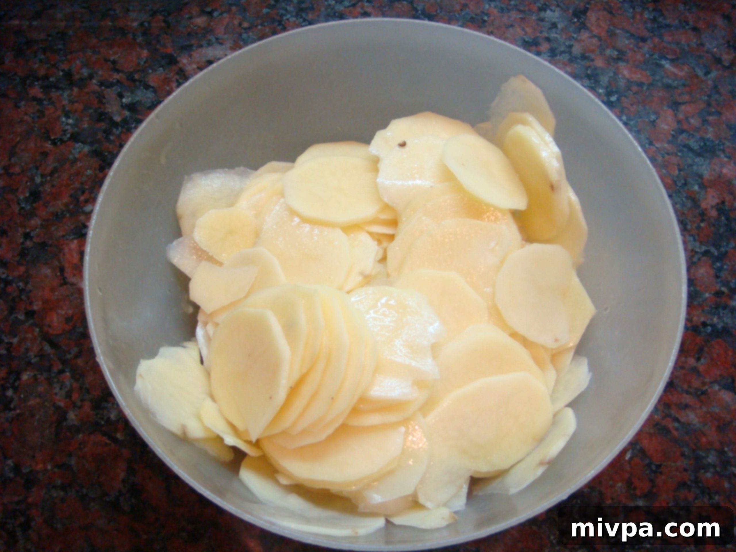 Hand mixing thin potato slices with melted butter, salt, and pepper in a bowl