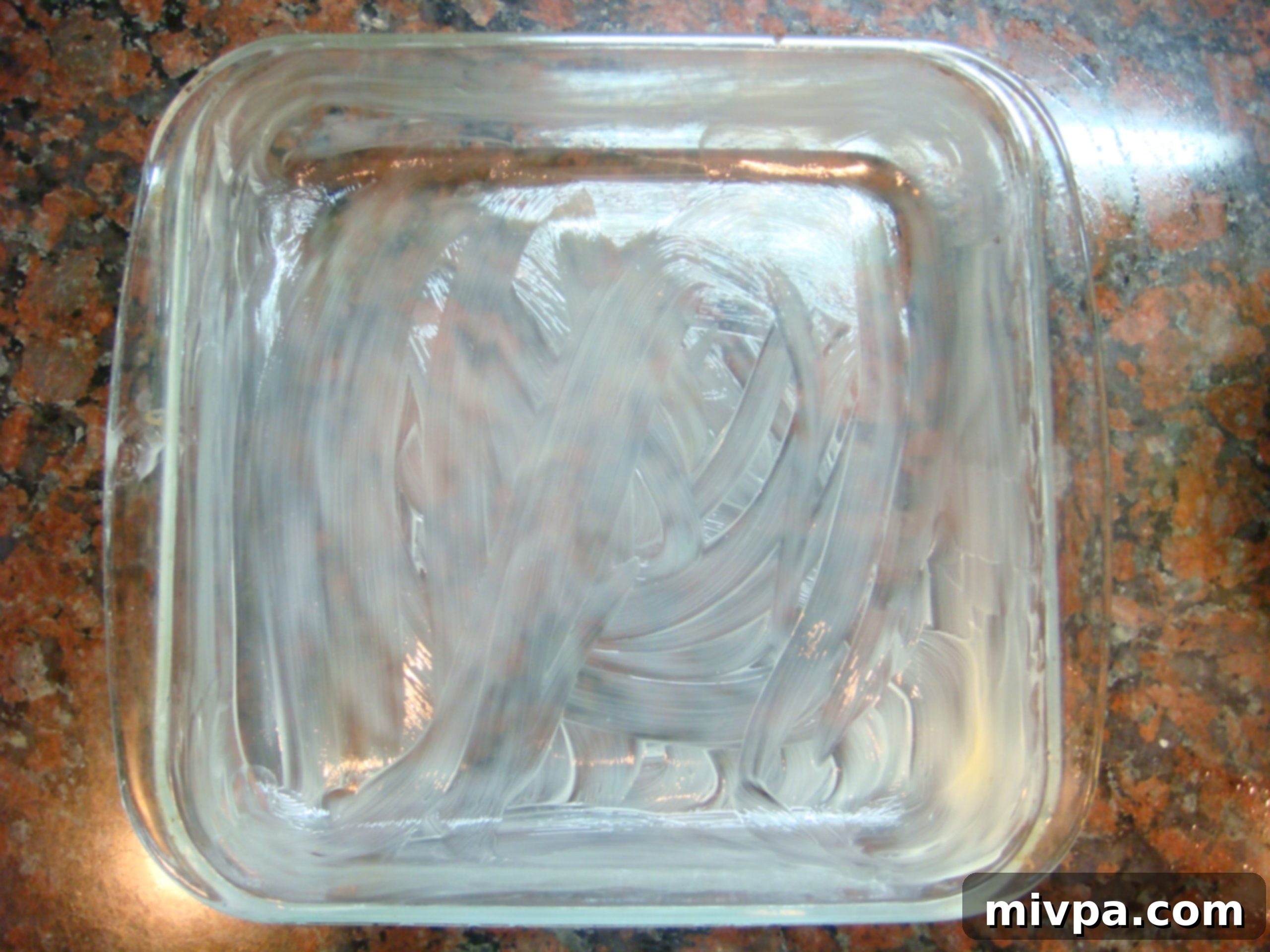 Glass baking pan being greased with butter, preparing for potato layers