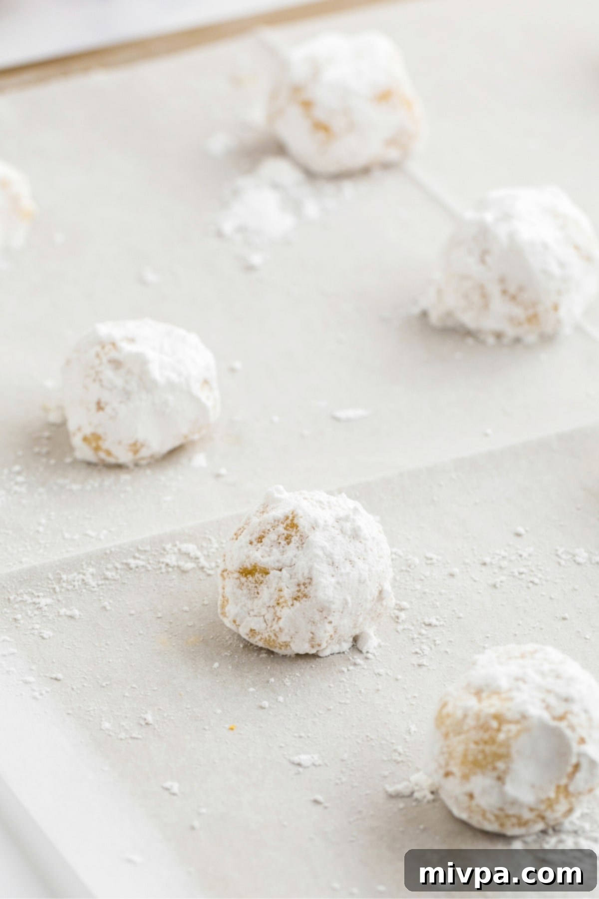 Dough balls rolled in powdered sugar on parchment paper.