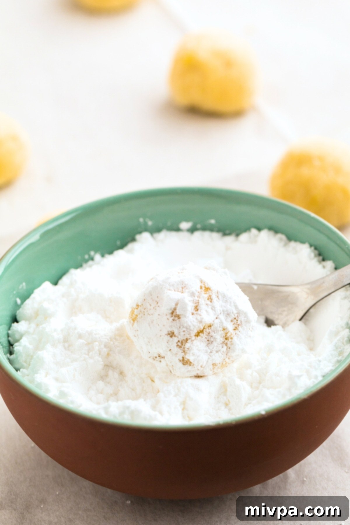 Rolling lemon cookie dough balls in powdered sugar.