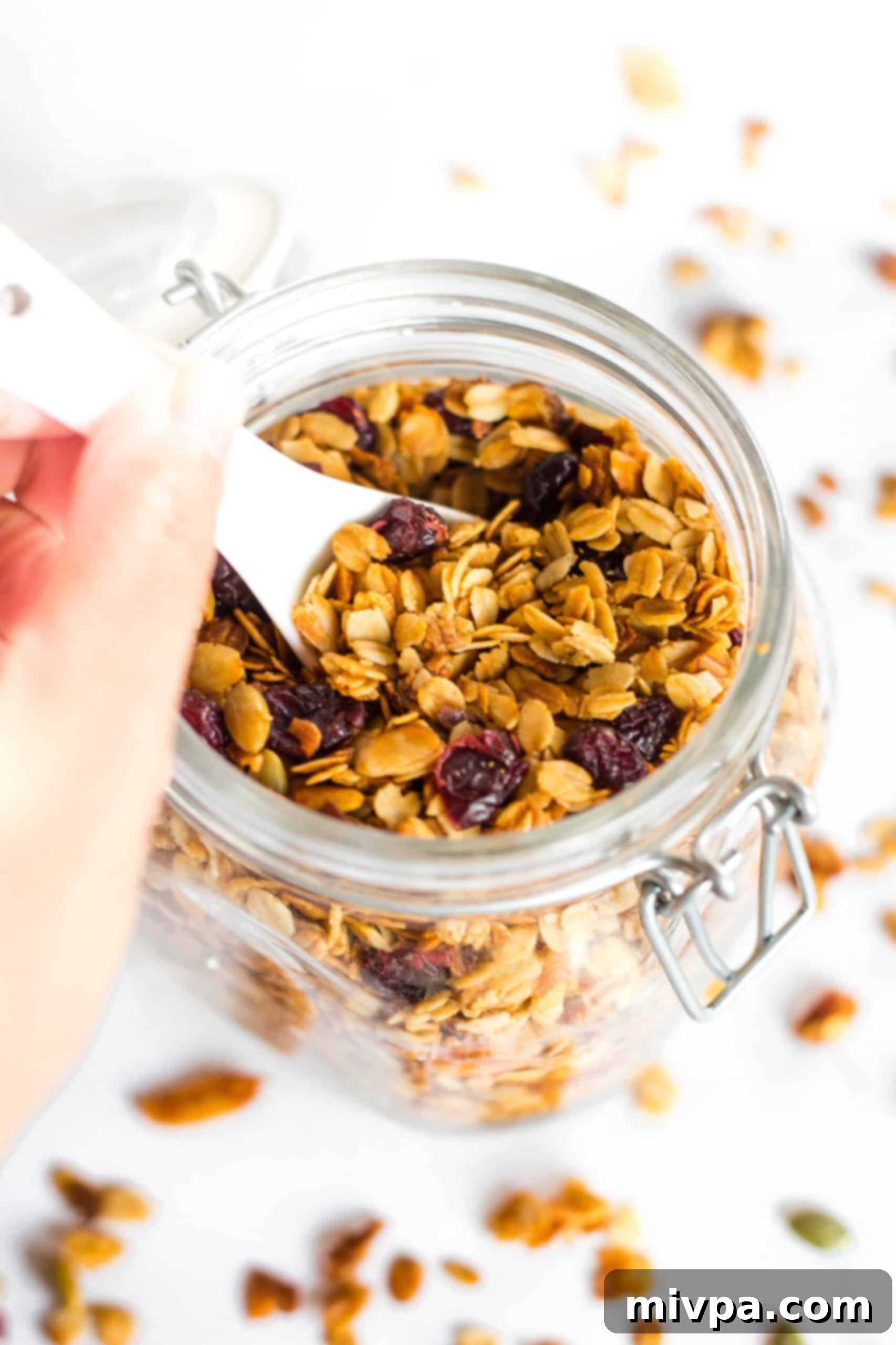 Homemade Gluten-Free Granola (Vegan) Reaching for a spoonful of homemade gluten-free granola from a jar.