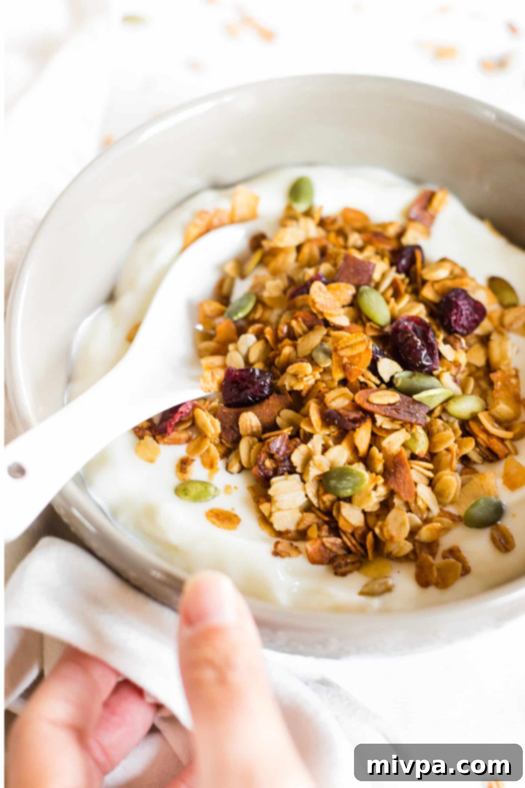 Gluten-Free Dairy-Free Granola Recipe Holding a bowl of granola topped yogurt.