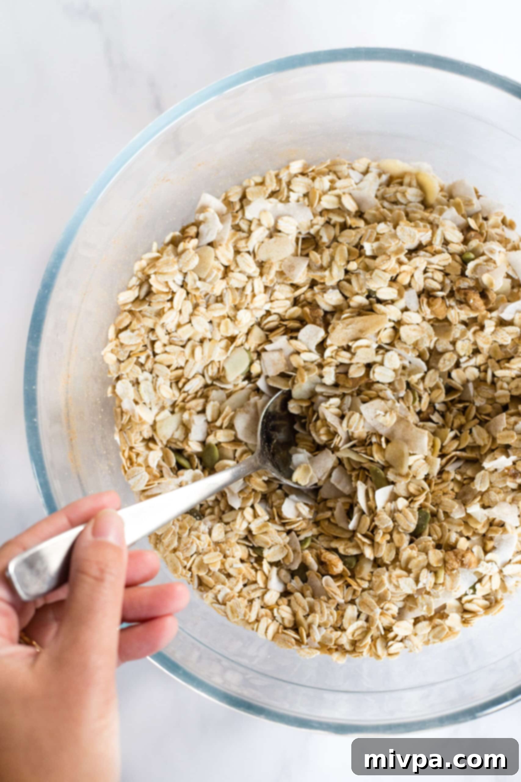Gluten-Free Dairy-Free Granola Recipe Mixing oats, nuts and seeds in glass bowl.