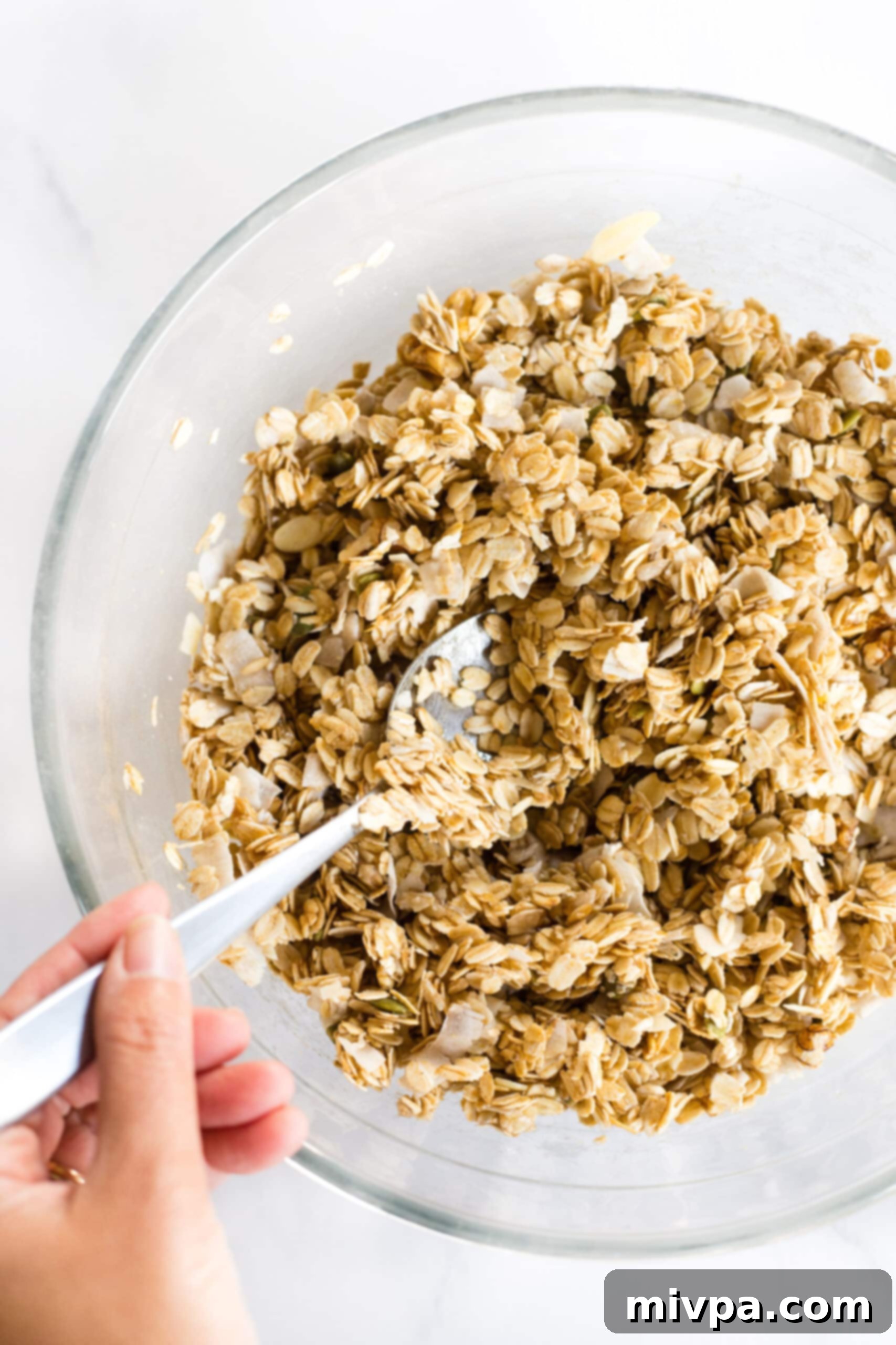 Gluten-Free Vegan Granola Mixing granola mixture in glass bowl.