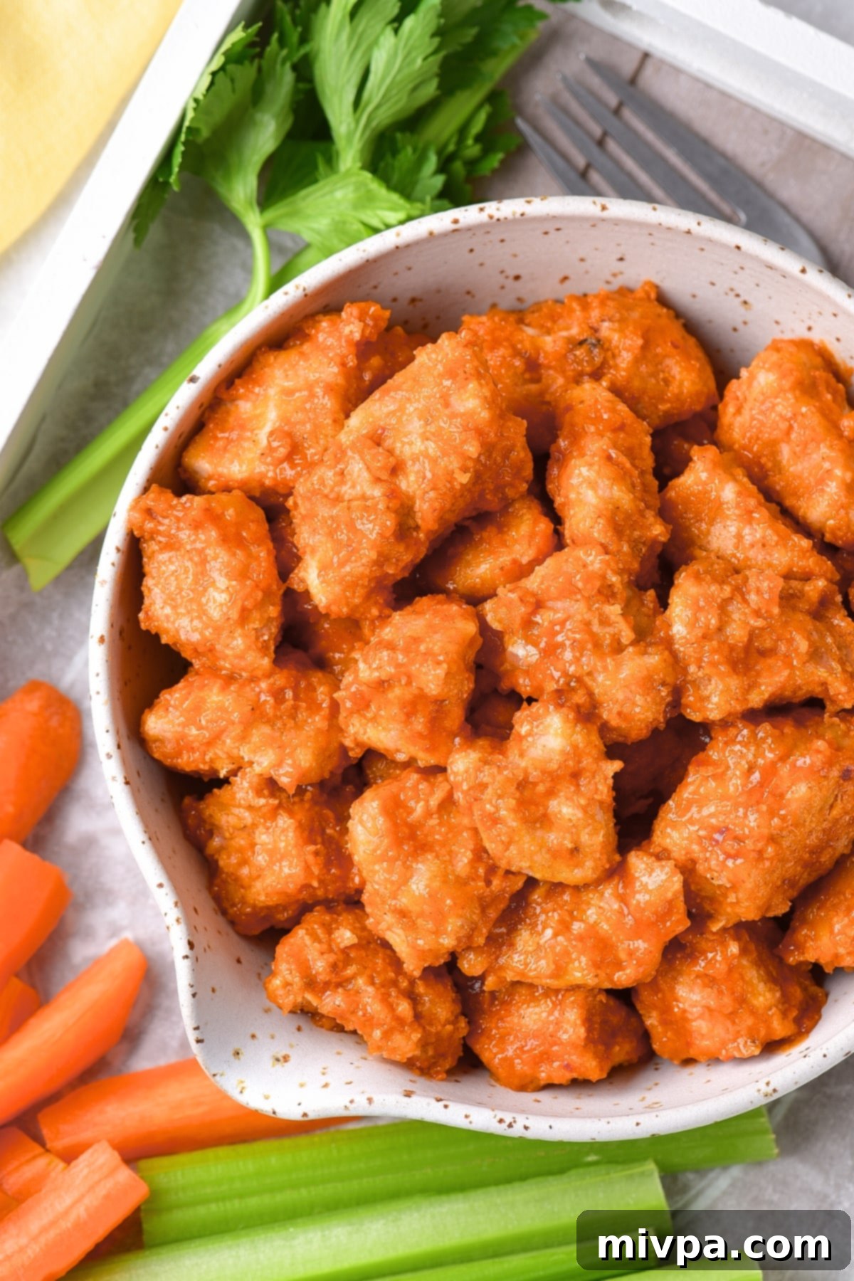 A bowl of air fryer buffalo chicken bites with veggies on tray.
