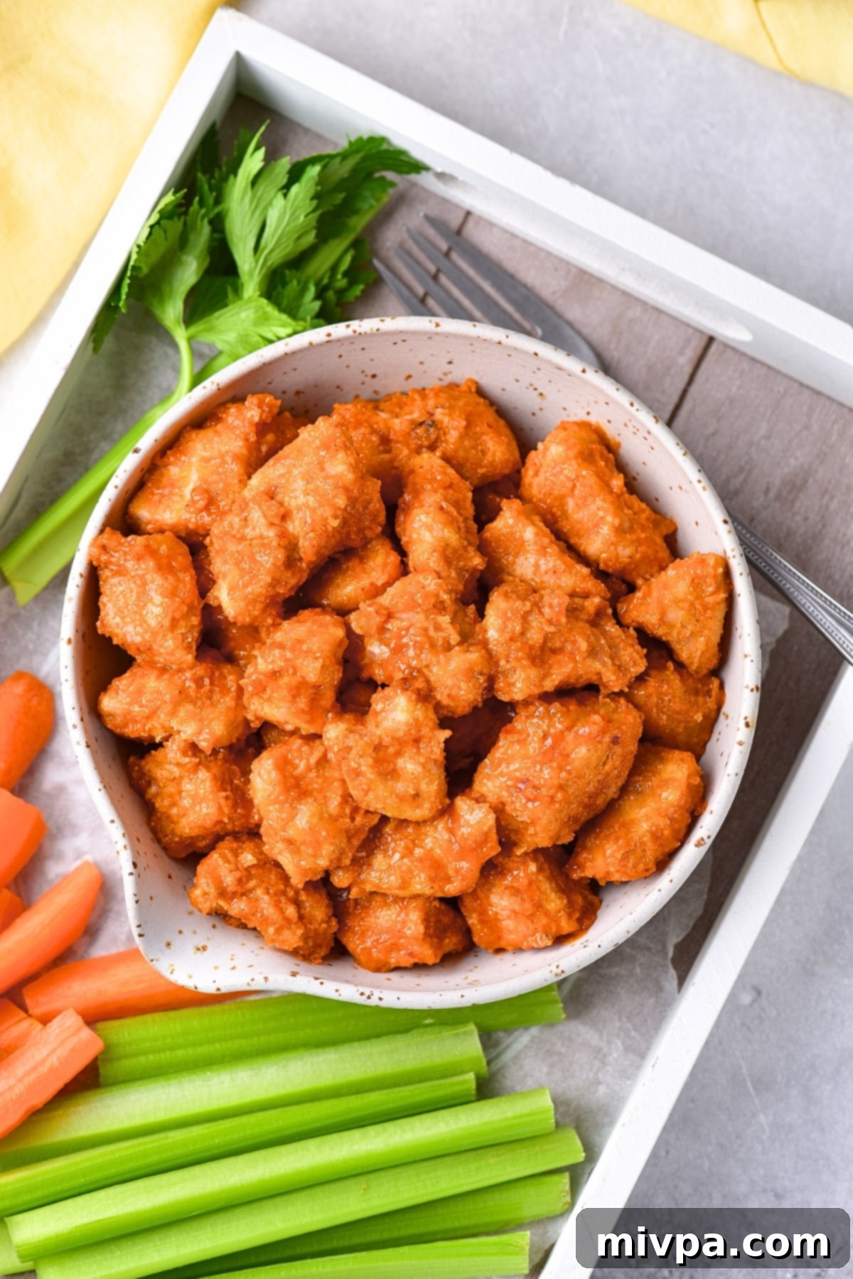 A bowl of buffalo chicken bites and carrot sticks and celery sticks.