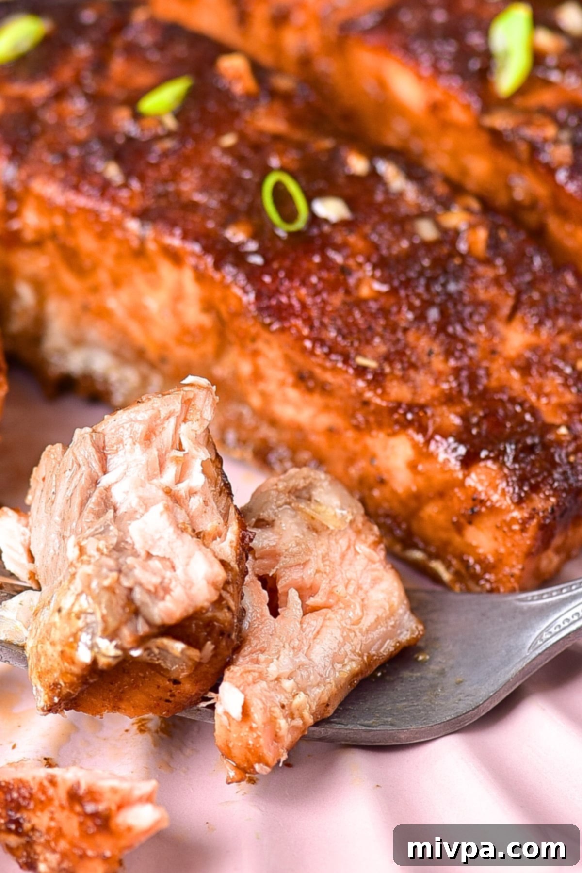 A fork holding a piece of half-eaten spicy firecracker salmon, showcasing its flaky texture and vibrant glaze.