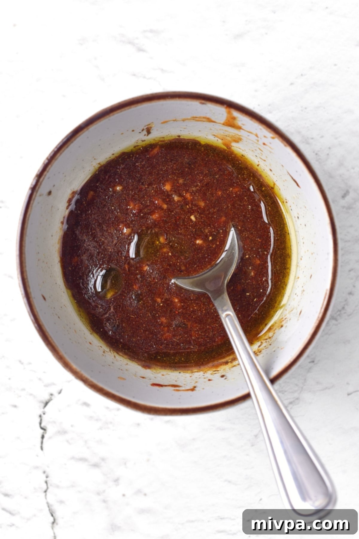 A spoon resting in a bowl filled with the vibrant, freshly mixed spicy firecracker sauce, ready for marination.