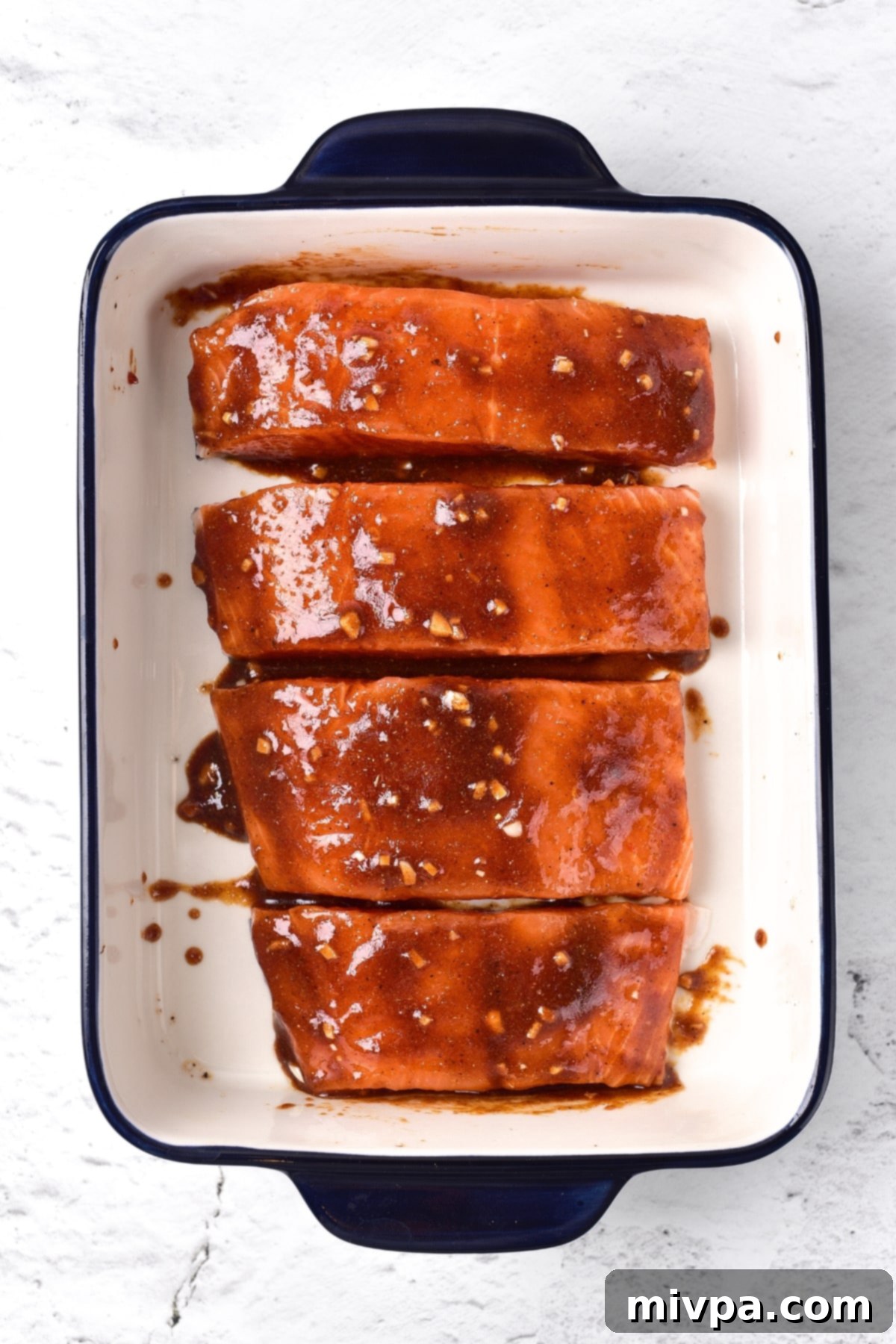 Fresh salmon fillets soaking in the rich, red firecracker sauce inside a baking dish, marinating for flavor.