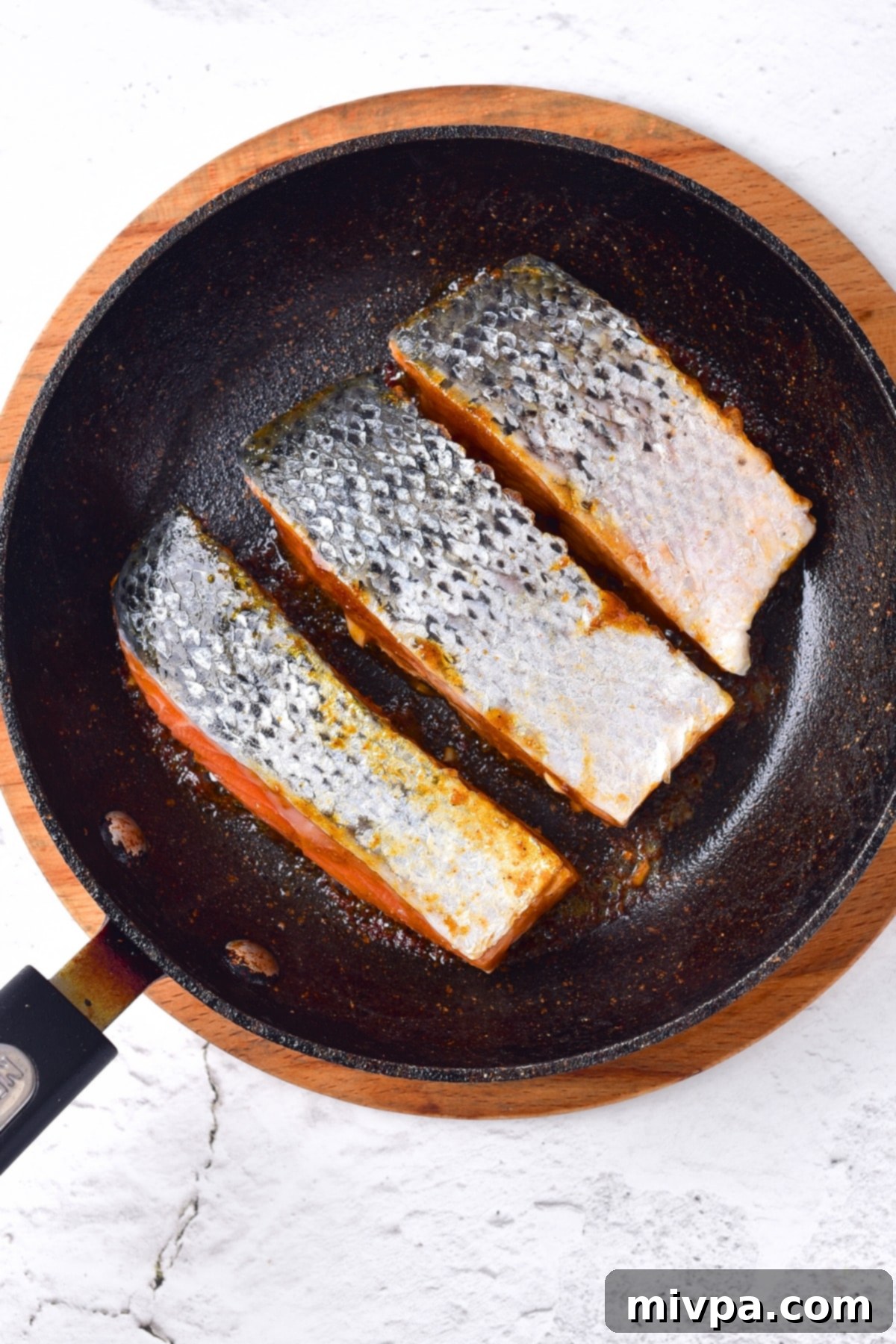 Two salmon fillets being seared skin side up in a hot skillet, developing a delicious crust.