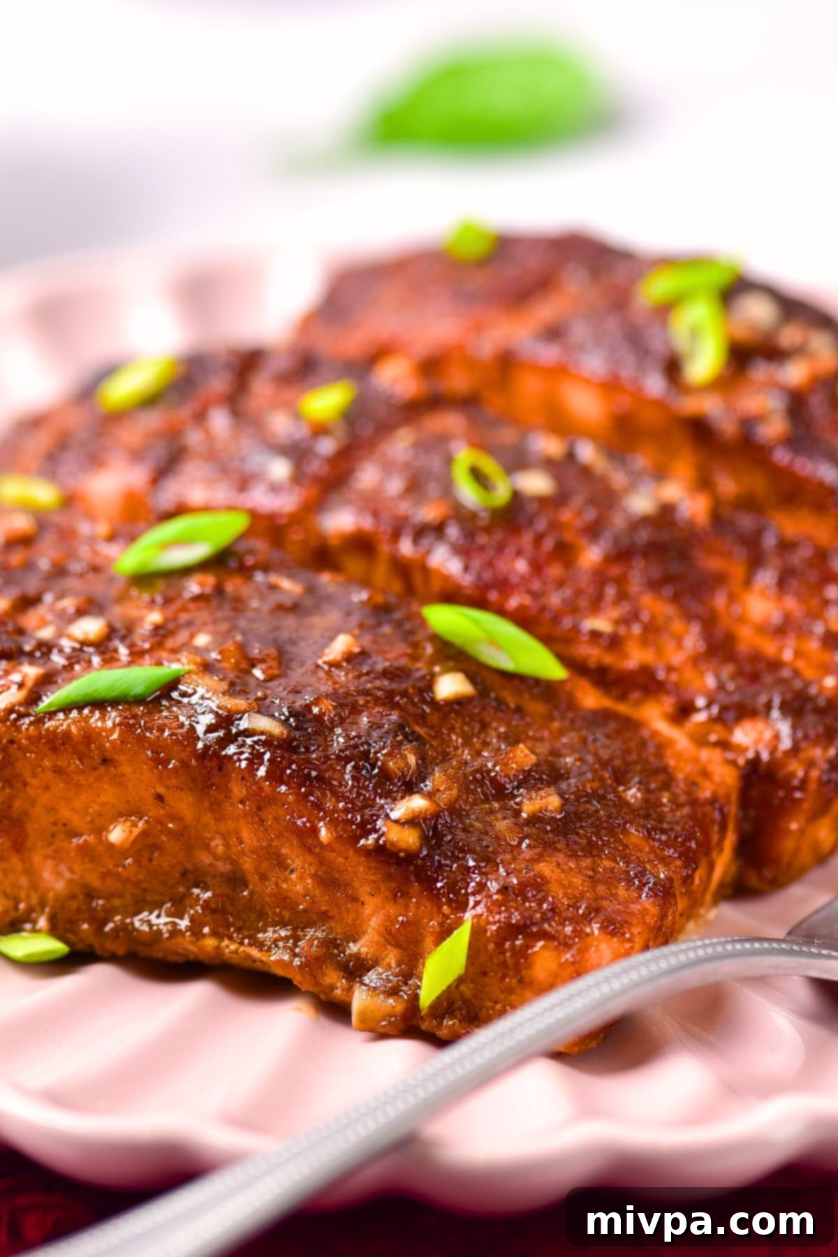 A close-up view of two perfectly baked salmon fillets, rich with firecracker sauce, garnished and presented on a plate.