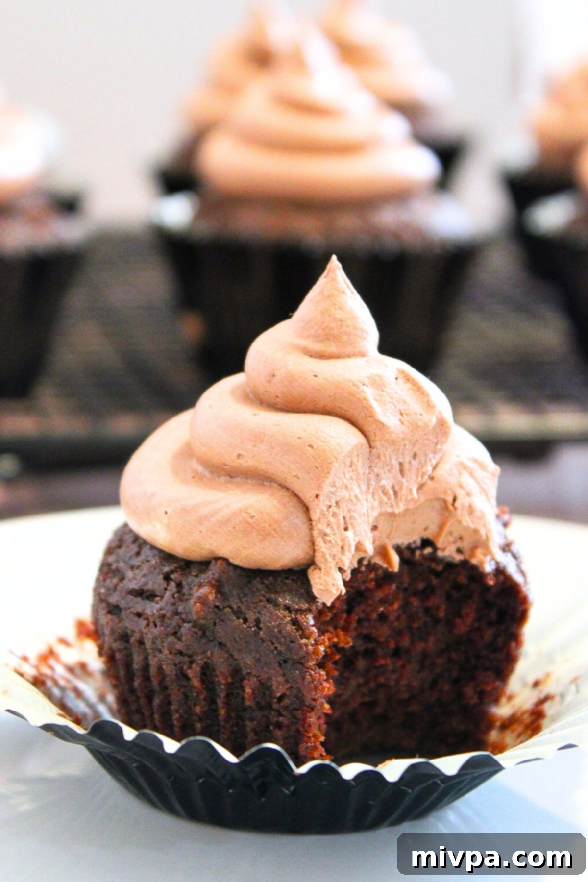 Half-eaten gluten-free chocolate cupcake in cupcake liner, showcasing its moist texture and rich chocolate color.