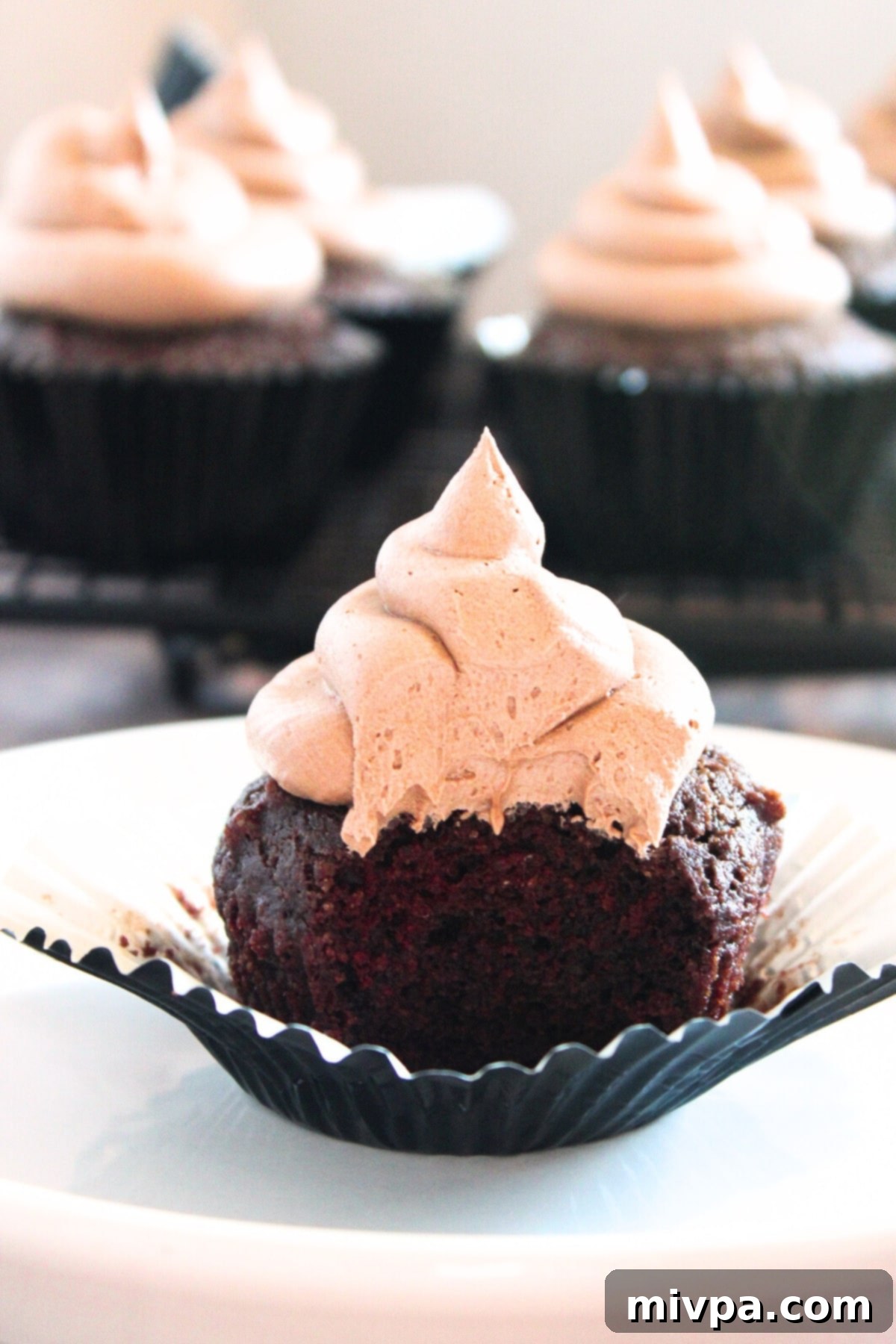 Close-up of a half-eaten vegan gluten-free chocolate cupcake in its liner, showing the light, airy crumb and rich frosting.
