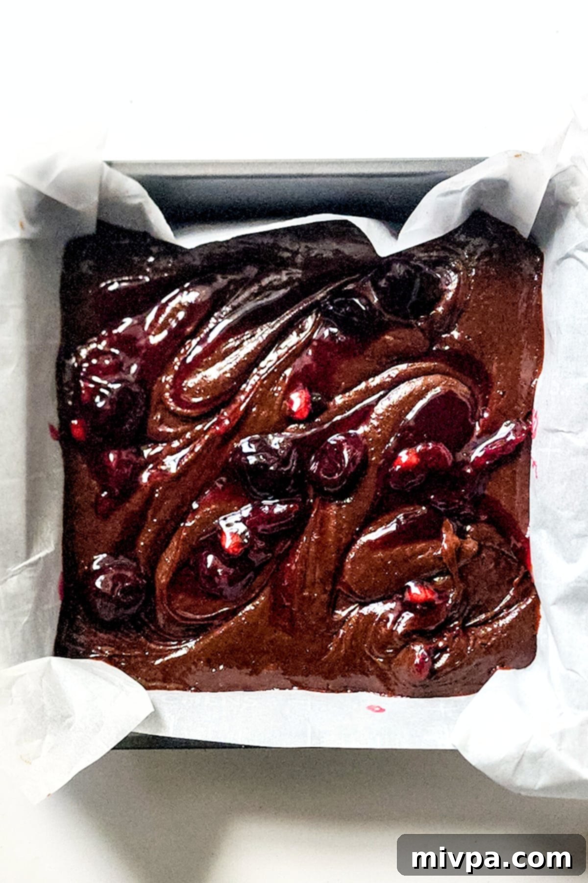 Gluten-Free Black Forest Brownies A beautifully swirled pattern of red cherry sauce infused into rich chocolate brownie batter within a baking pan, creating a marbled effect.