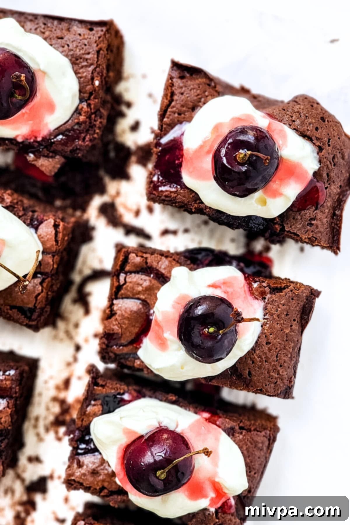 Simple Allergy Friendly Black Forest Brownies 2 An inviting top-down view of several Black Forest brownies, beautifully topped with dairy-free whipped cream and fresh cherries, arranged on a serving plate.