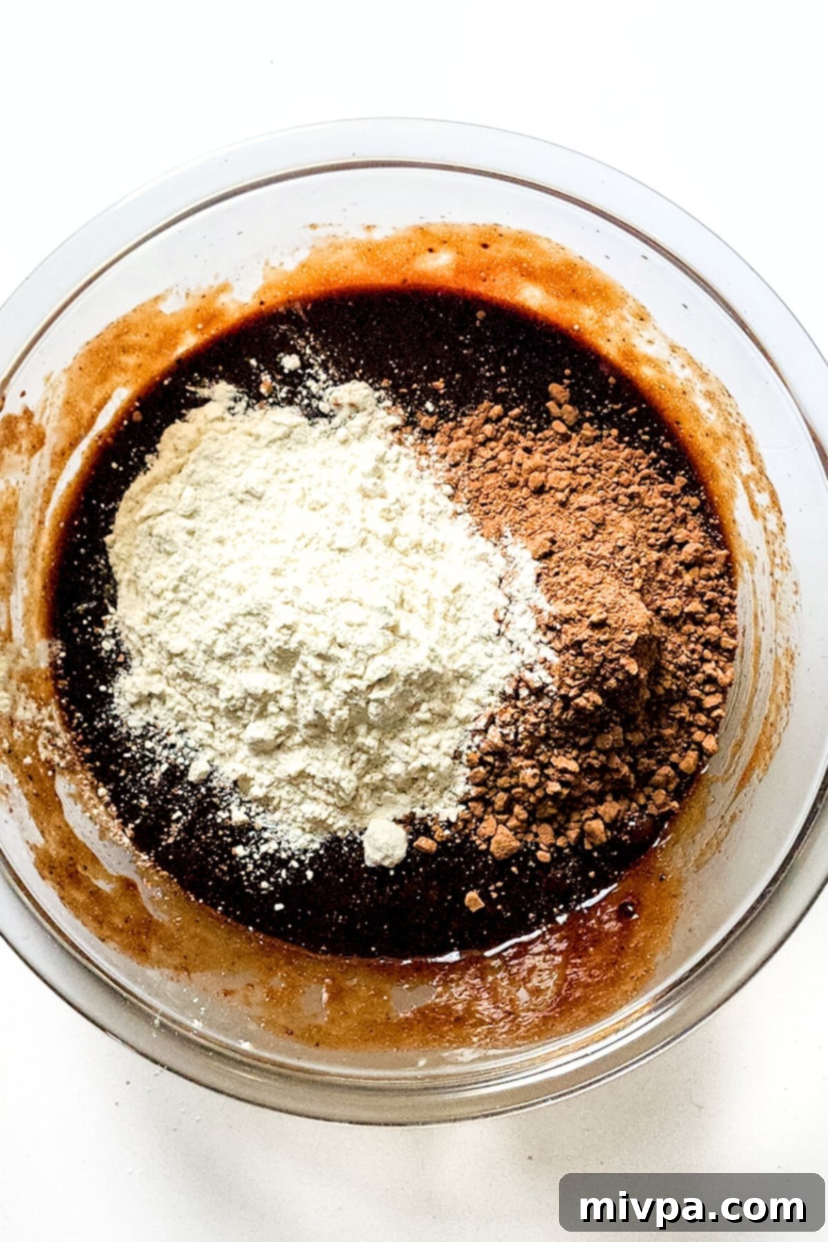 Easy Black Forest Brownie Recipe (Gluten-Free, Dairy-Free) Dry ingredients (flour, cocoa powder, espresso powder) piled on top of the wet chocolate brownie mixture in a glass bowl, ready to be folded in.
