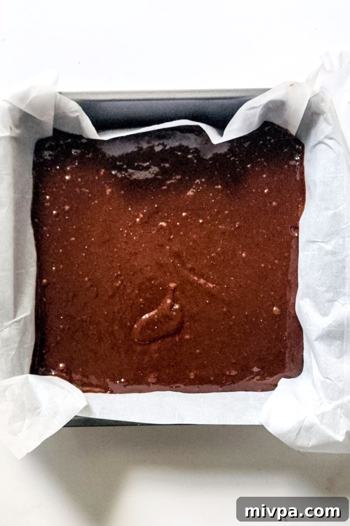 Fudgy Black Forest Brownies (Gluten-Free, Dairy-Free) Thick chocolate brownie batter spread evenly in a parchment-lined square baking pan, ready for the cherry swirl.