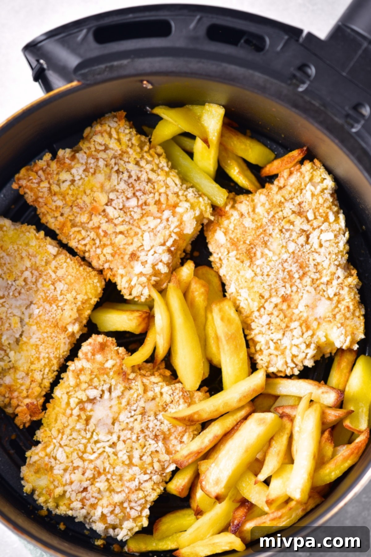 Top down view of crispy gluten-free fish and chips in an air fryer basket, perfectly cooked.