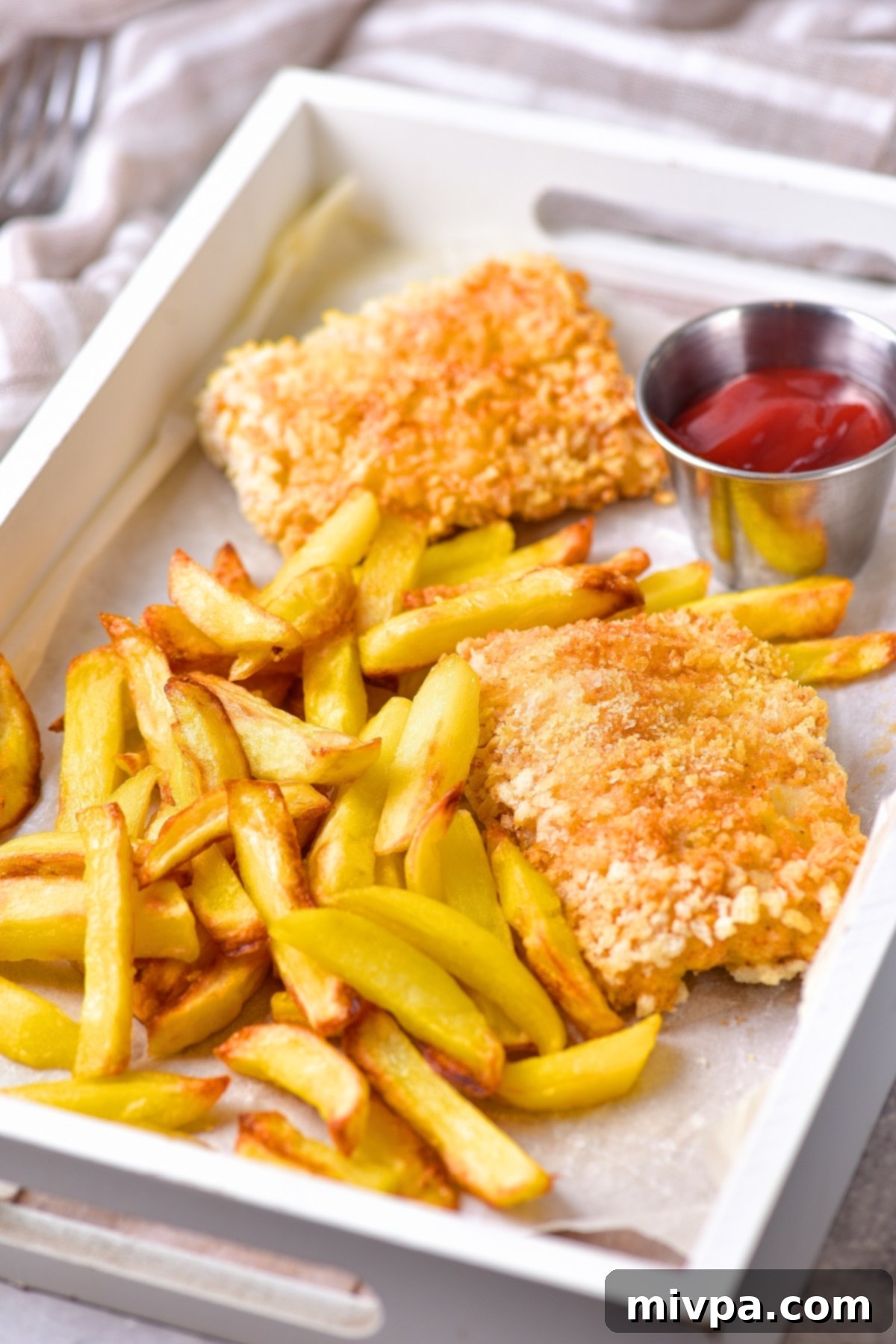 Gluten-free fish and chips cooked in an air fryer, served on a parchment-lined tray with lemon.
