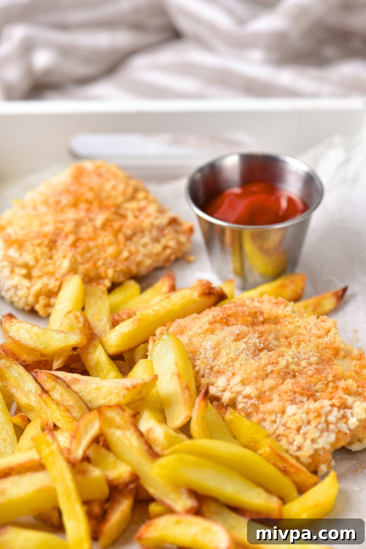 Close up view of golden fried gluten-free fish and chips on a parchment-lined tray, ready to serve.