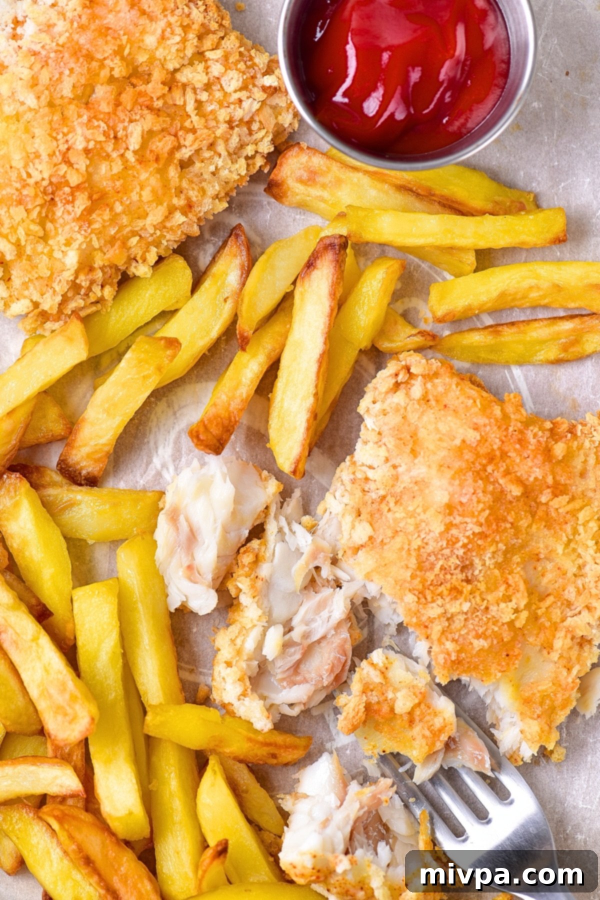 Top down view of a half-eaten plate of gluten-free fish and chips with lemon and sauce.