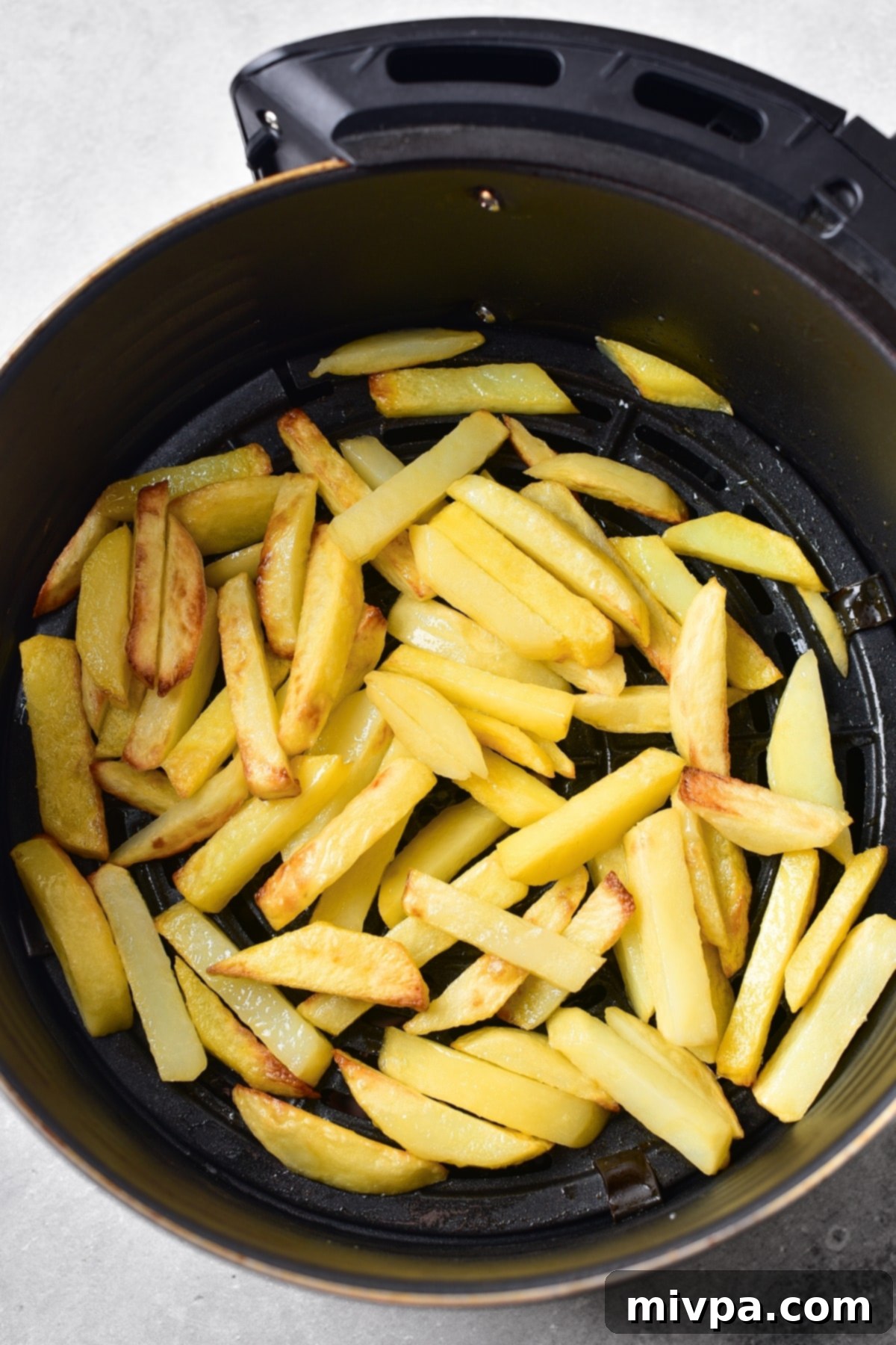 Sliced potatoes cooking in an air fryer basket.