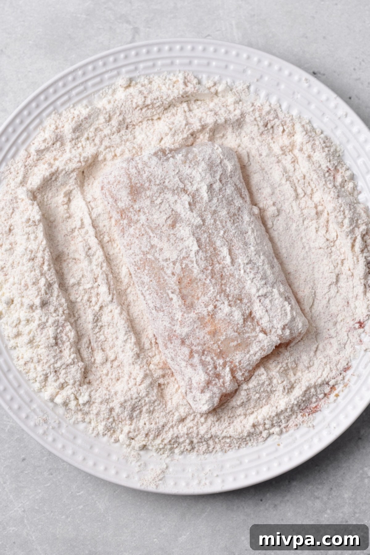 Coating cod fish fillets in a seasoned gluten-free flour mixture in a bowl.