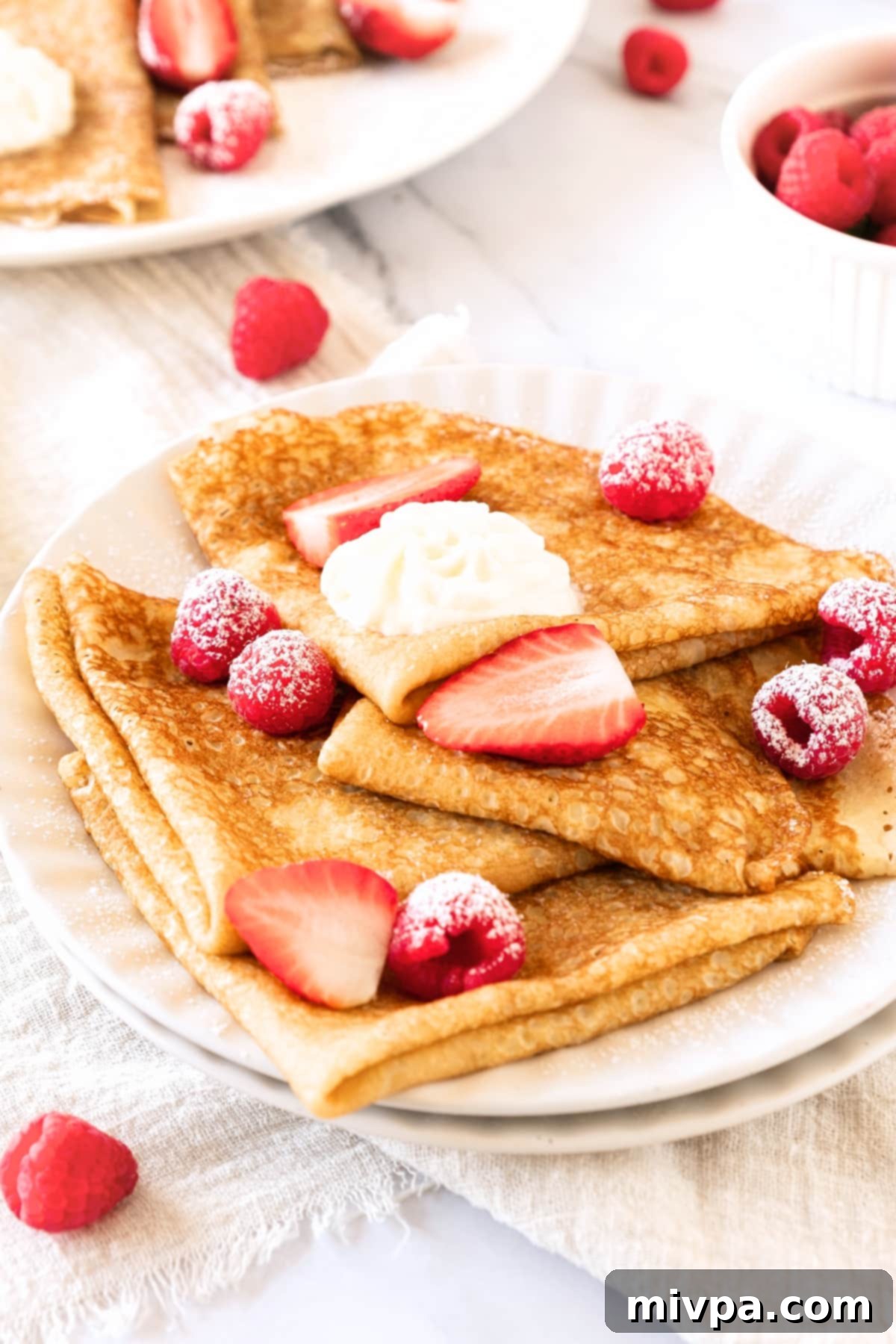 A plate of gluten-free crepes topped with berries and cream.