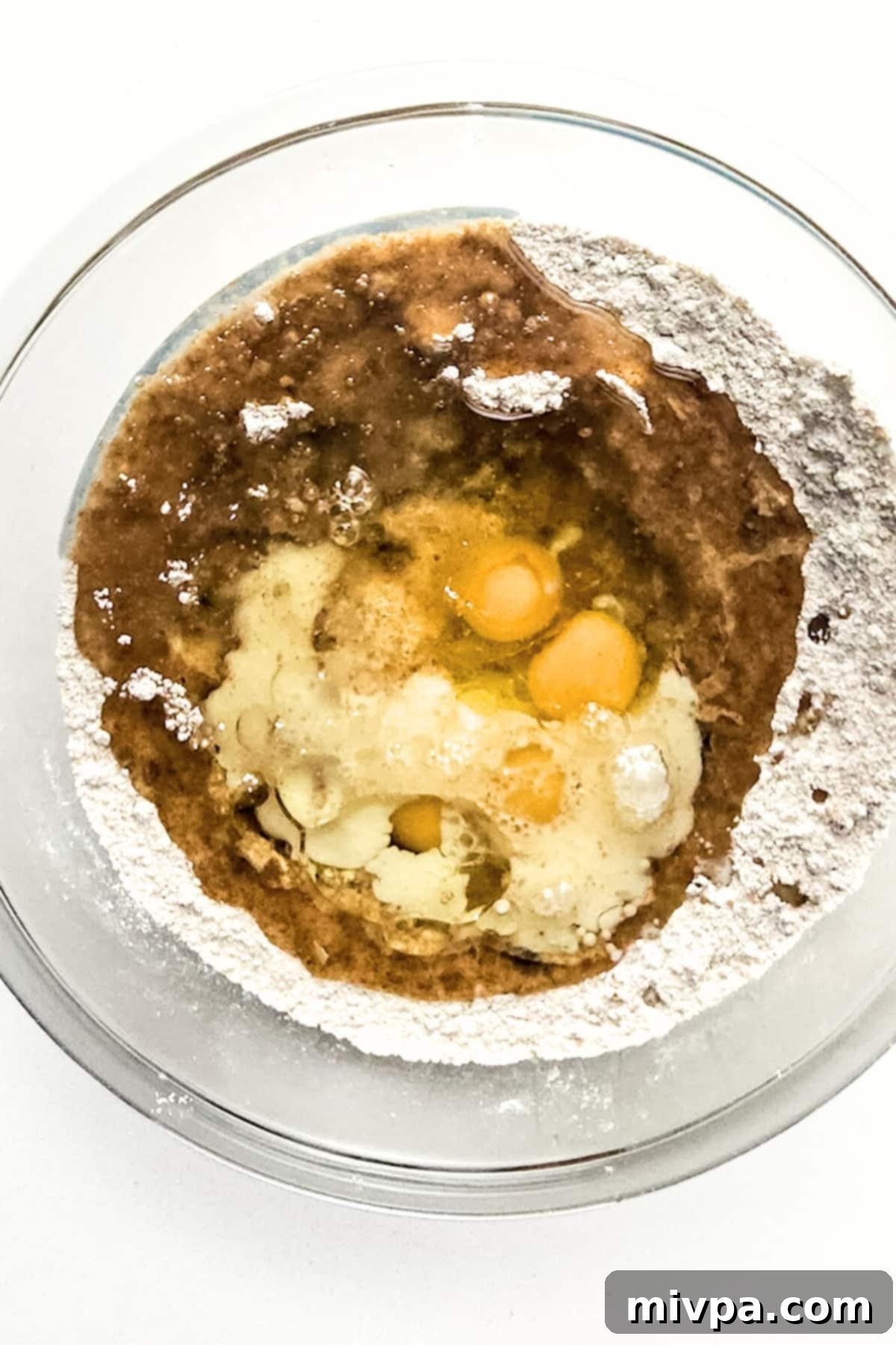 Gluten and Dairy Free Carrot Cake Wet ingredients on top of dry ingredients in glass bowl.