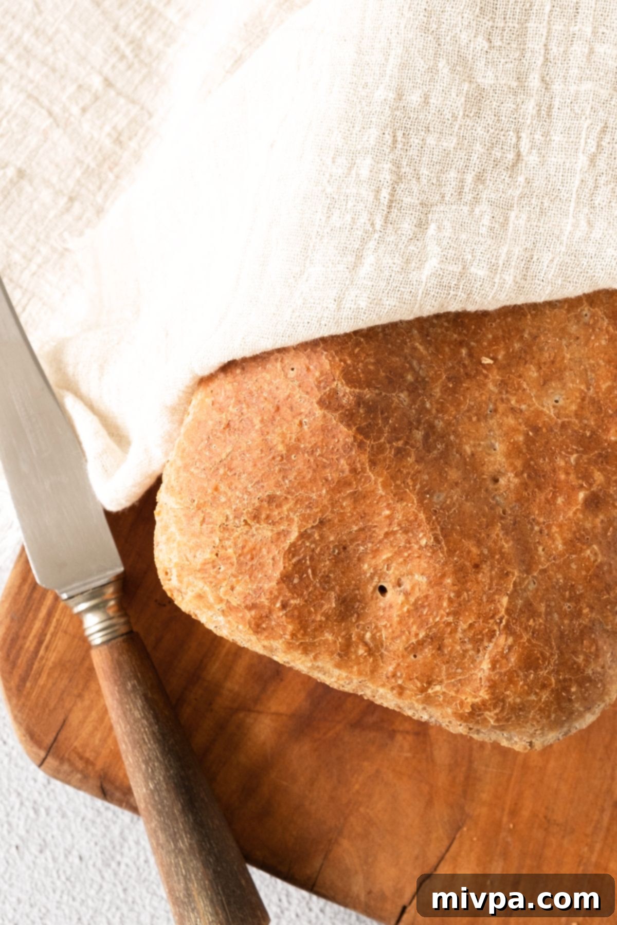GF Bread Recipe with Beer Top-down view of a freshly baked gluten-free bread loaf covered in a clean kitchen towel, cooling on a wire rack.