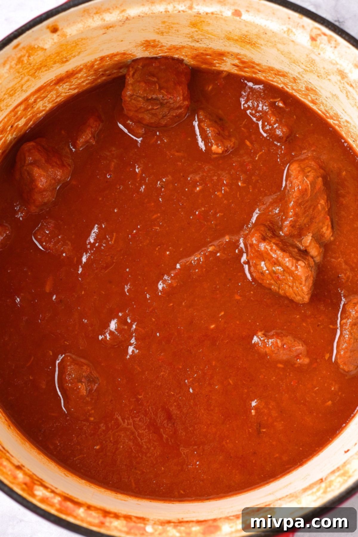Slow cooked beef resting in the rich red sauce after cooking.