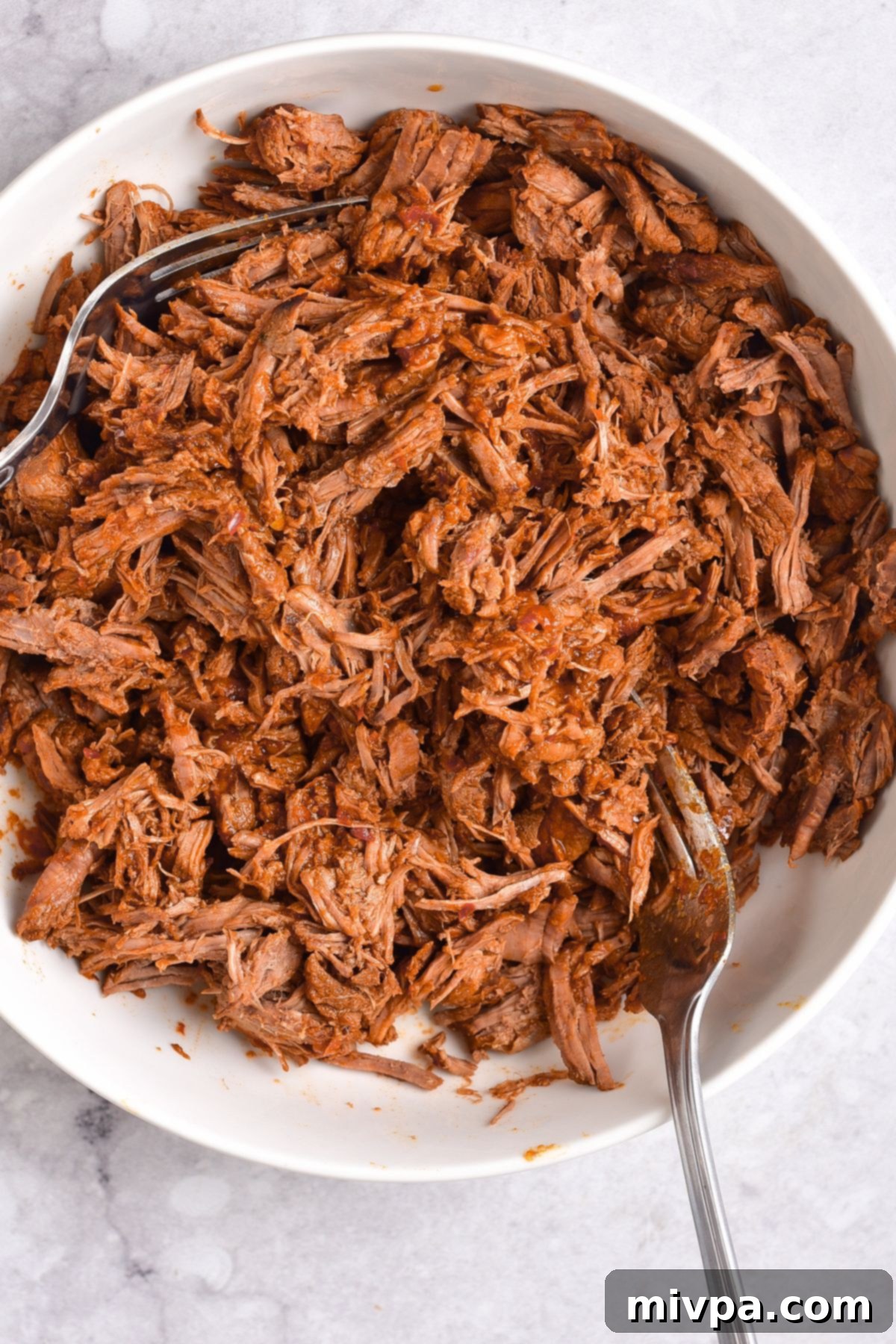 Shredding beef with two forks, showing its tender texture.