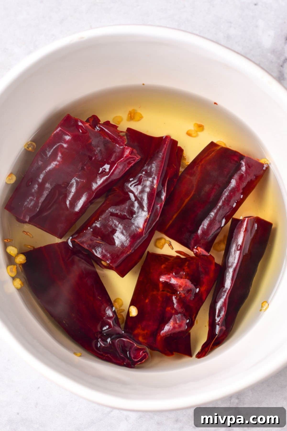 Soaking cut guajillo peppers in a bowl of hot water to rehydrate them.