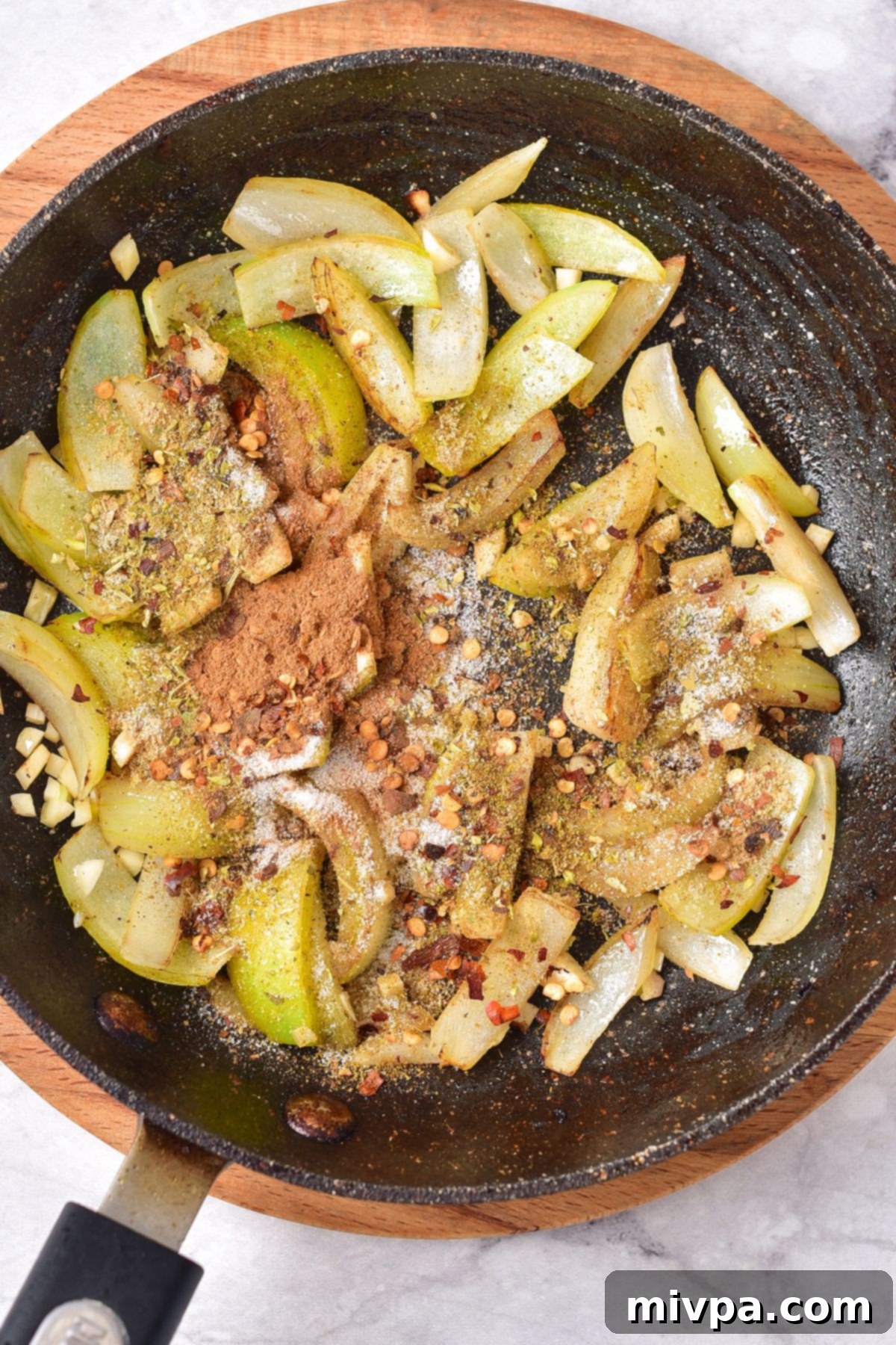 Sautéing sliced onions, garlic, and spices in a skillet, creating a fragrant base.