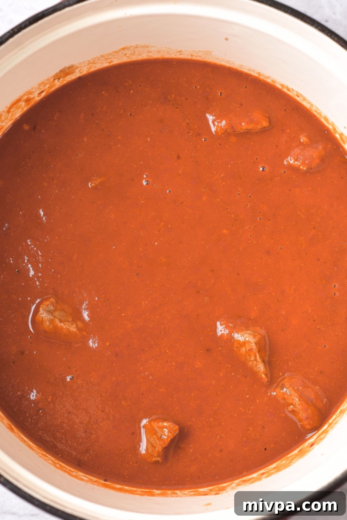 Beef pieces cooking in the rich red adobo sauce in a large pot.
