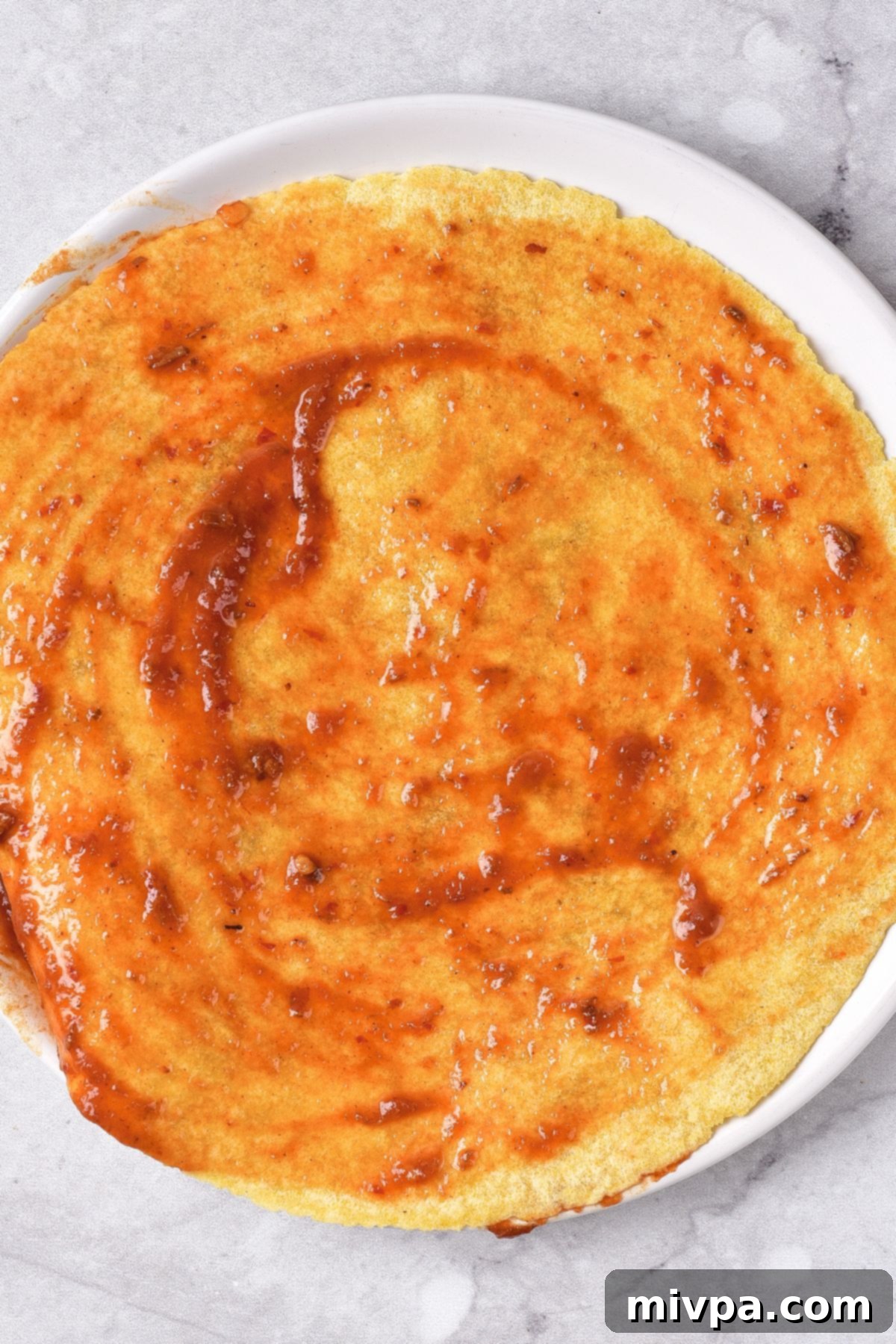 Corn tortilla being brushed with red birria sauce.