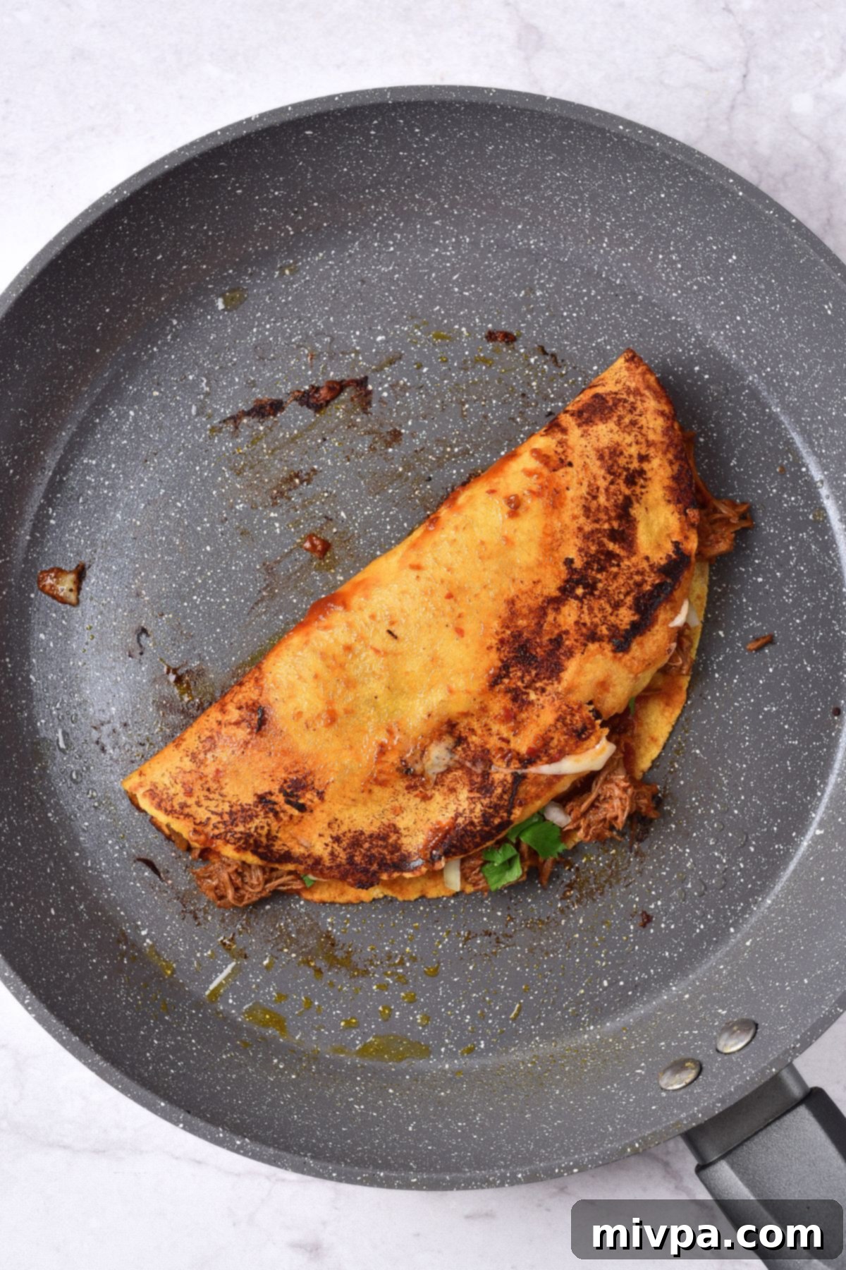Folding a taco in a nonstick skillet to melt the cheese.