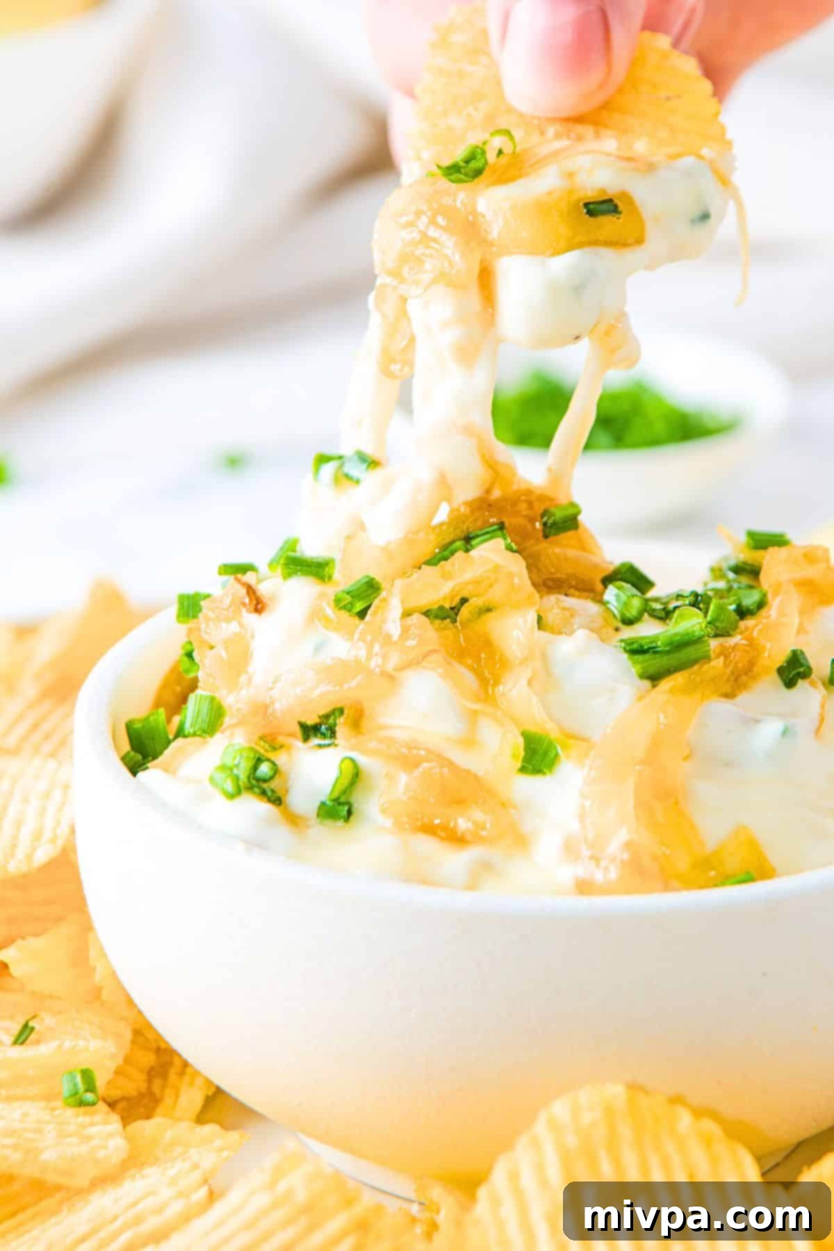 Homemade French Onion Dip (Gluten-Free) Dipping a chip into a bowl of caramelized onion dip.