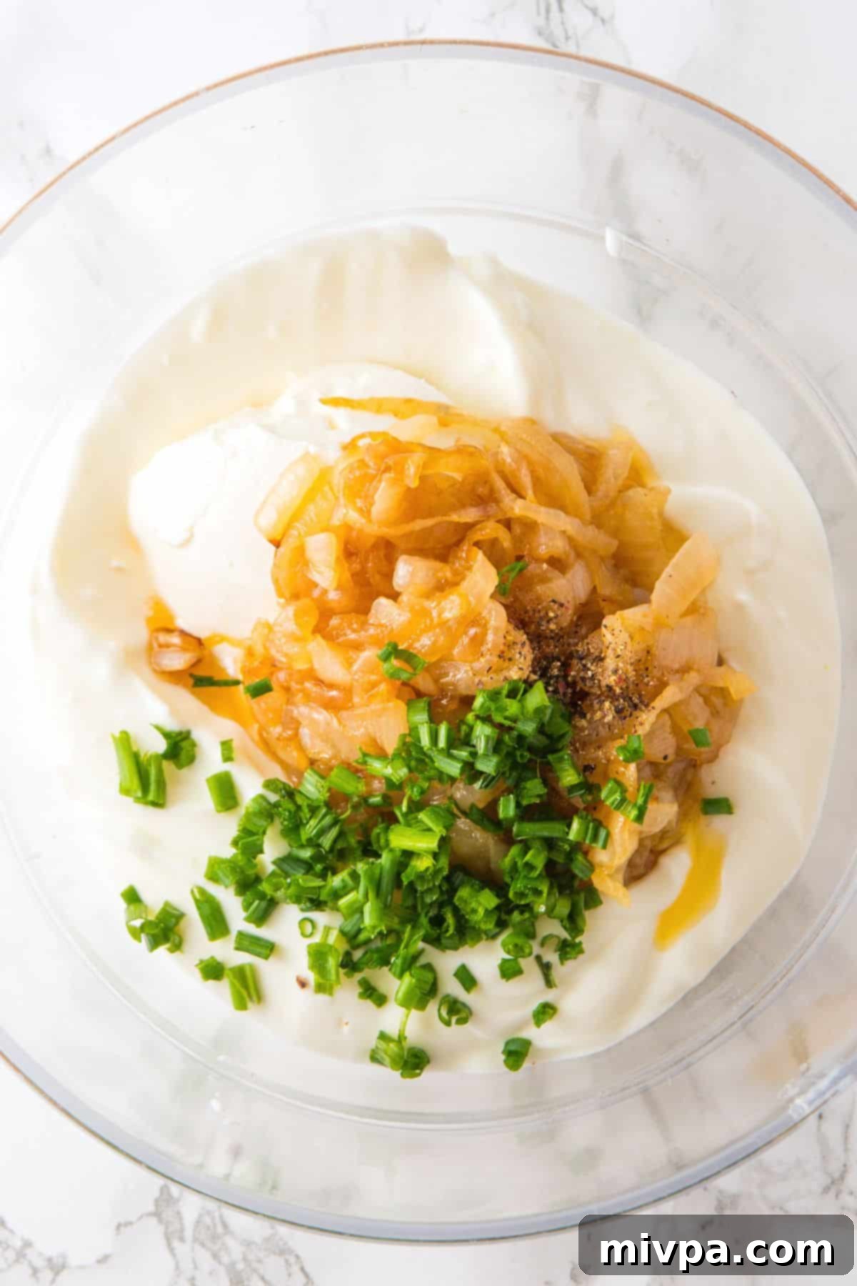 Homemade Onion Dip Recipe Caramelized onions, chopped chives, sour cream, and cheese cheese in glass bowl.
