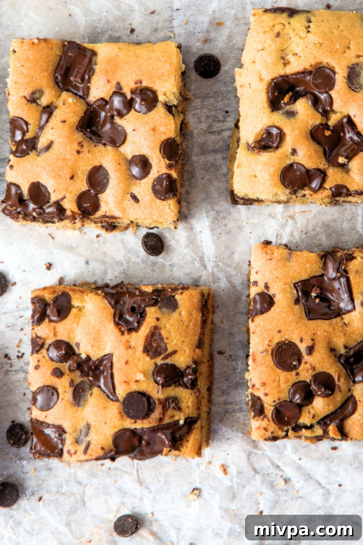 Gluten-Free Chocolate Chip Cookie Bars (Dairy-Free) - Top View Top down view of golden-brown gluten-free chocolate chip cookie bars on parchment paper, studded with melted chocolate.