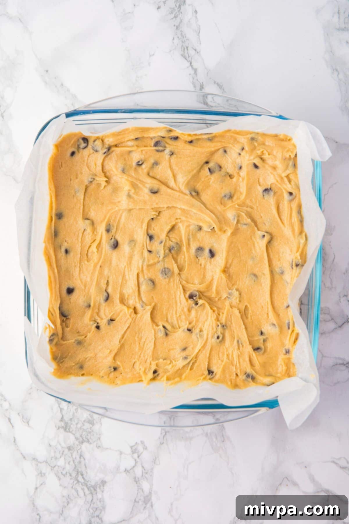 GF Cookie Bars with Chocolate Chips in Pan Chocolate chip cookie dough spread evenly in a parchment-lined baking pan.
