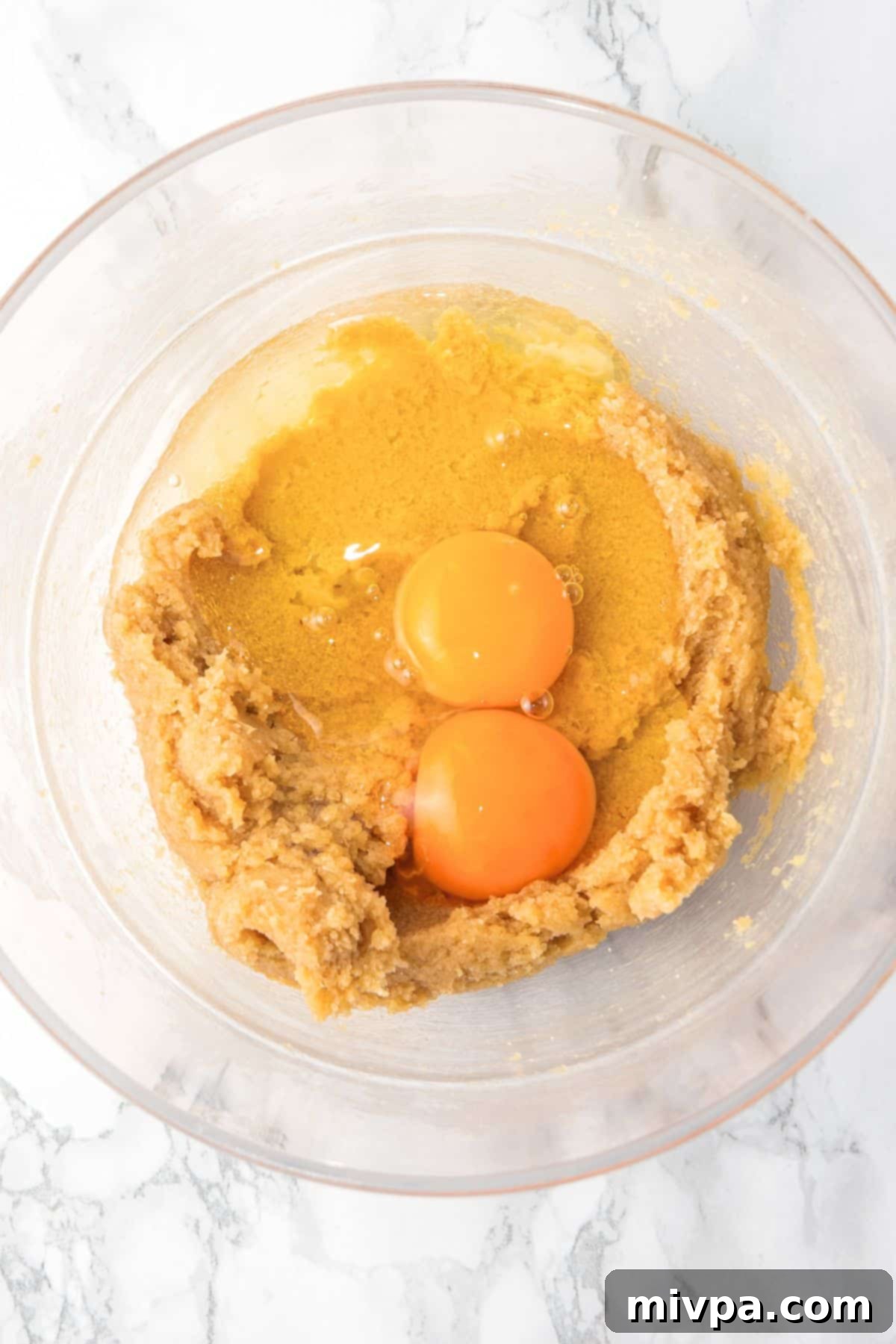 Gluten-Free Dairy-Free Chocolate Chip Bars - Eggs Added Two eggs added to the butter-sugar mixture in a glass mixing bowl, ready to be beaten.