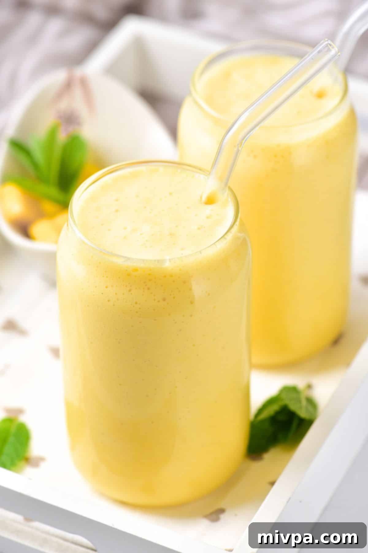 5-Ingredient Creamy Mango Milkshake Glasses of creamy mango milkshake, garnished with mint leaves, ready to be enjoyed on a warm day.