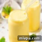 5 Malzemeli Kremalı Mango Milkshake 2 Mango milkshake garnished with mint leaves, served in a glass with a straw.