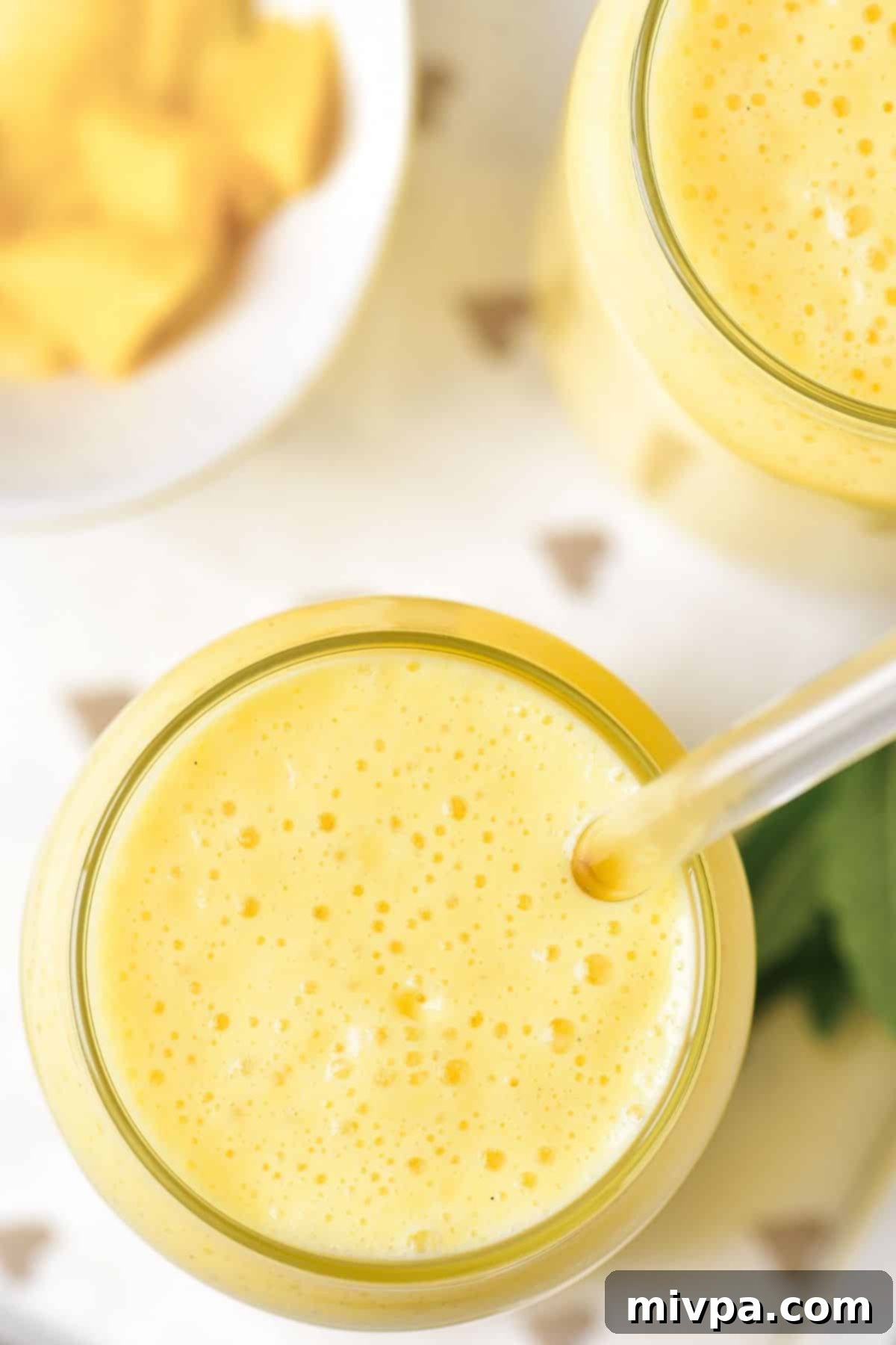 Creamy Mango Shake (Gluten-Free) Top down view of two glasses of creamy mango shake on a wooden table, garnished with fresh mint.