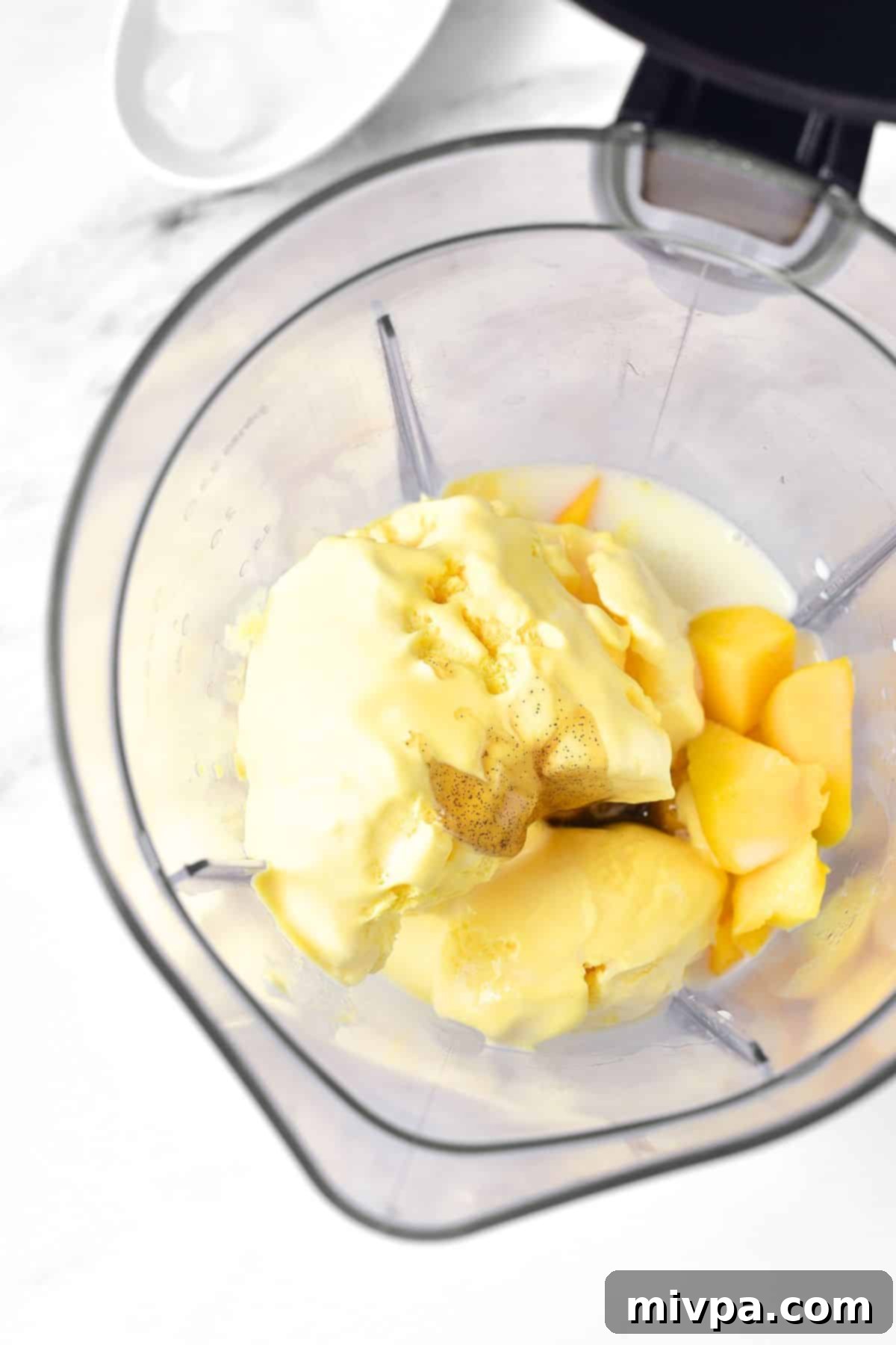 Gluten-Free Mango Milkshake Ice cream, diced mango, milk, and vanilla extract being added to a blender for the milkshake base.